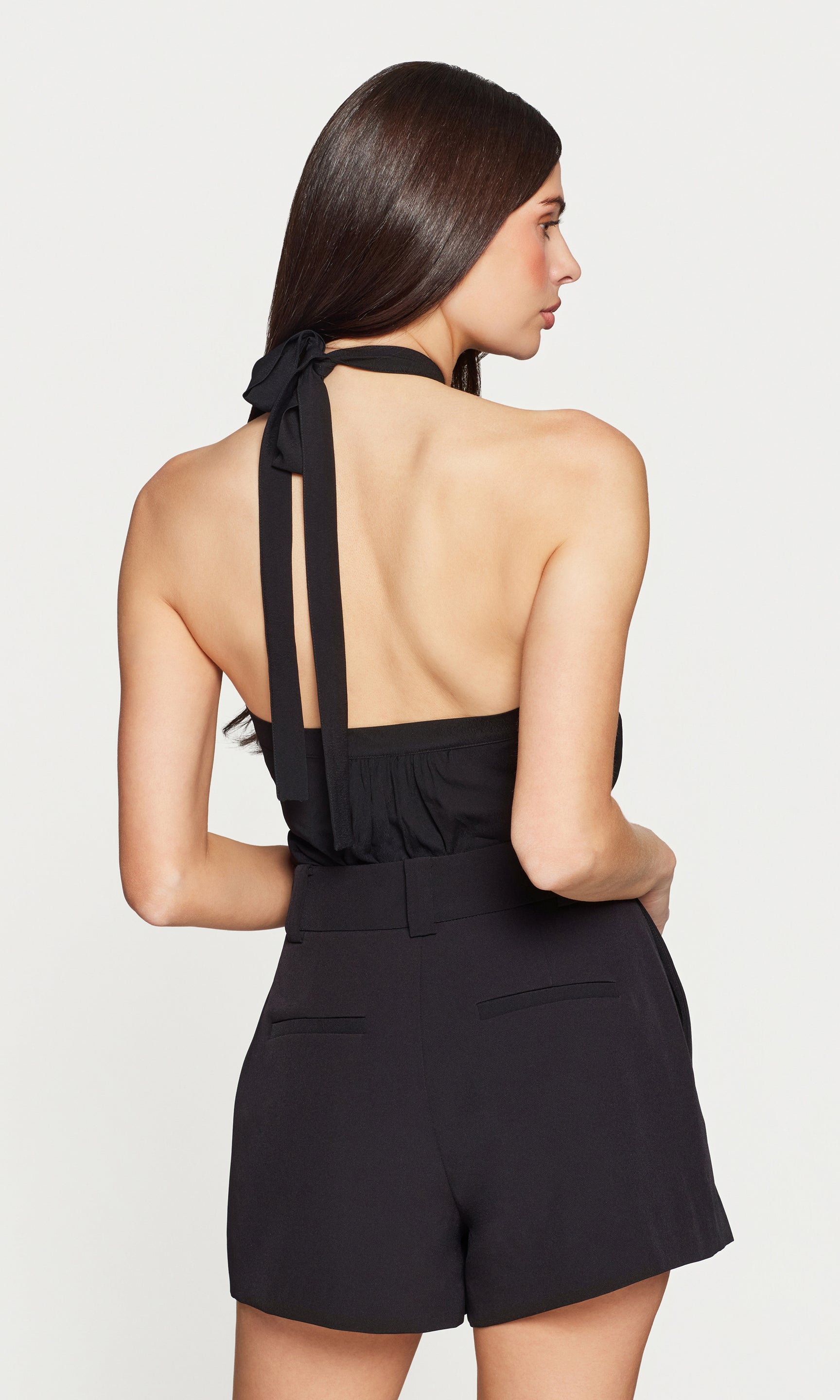 Back view of woman wearing a black halter neck top with tie straps on a white background