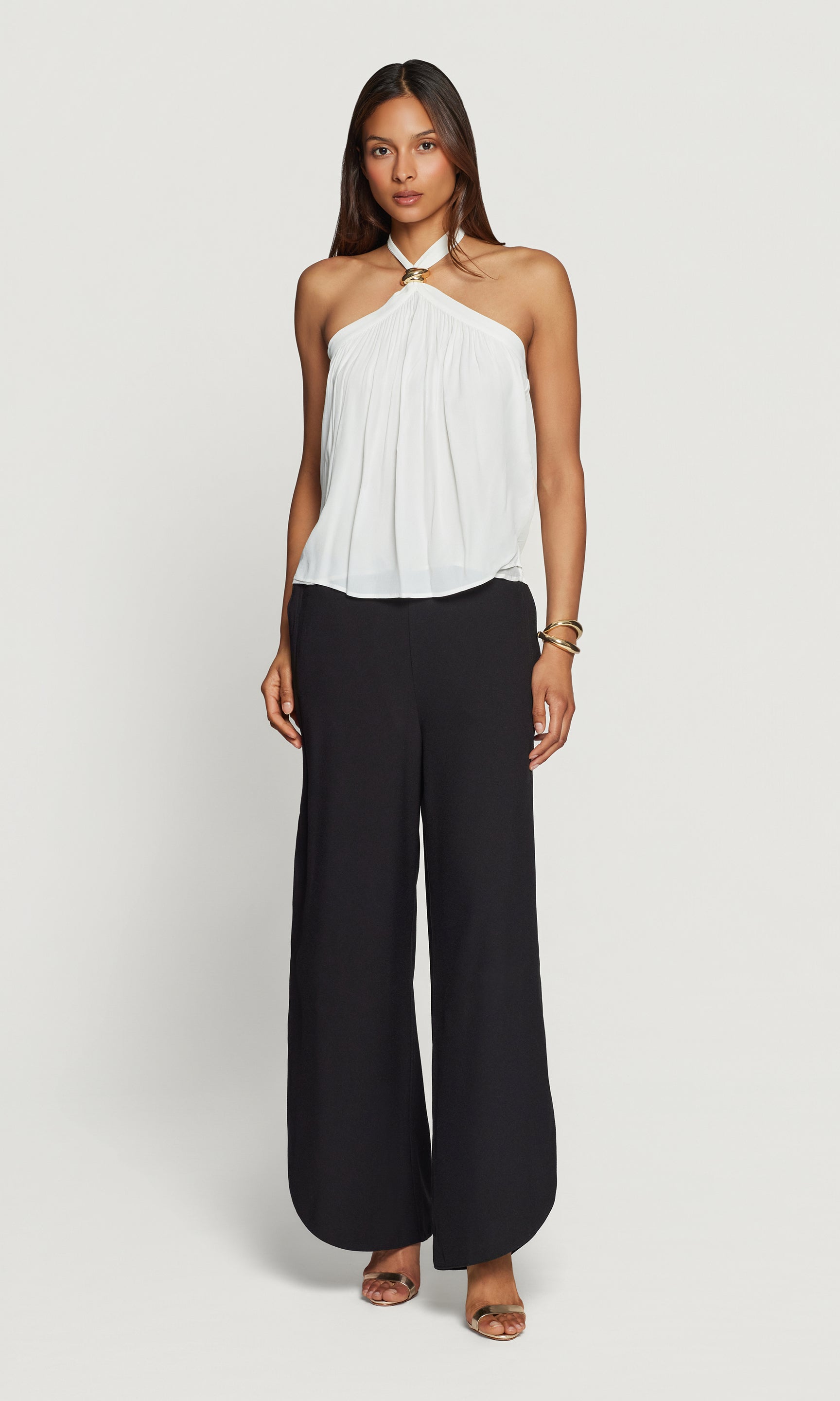 Woman wearing a white halter top and black wide-leg pants on a light gray background