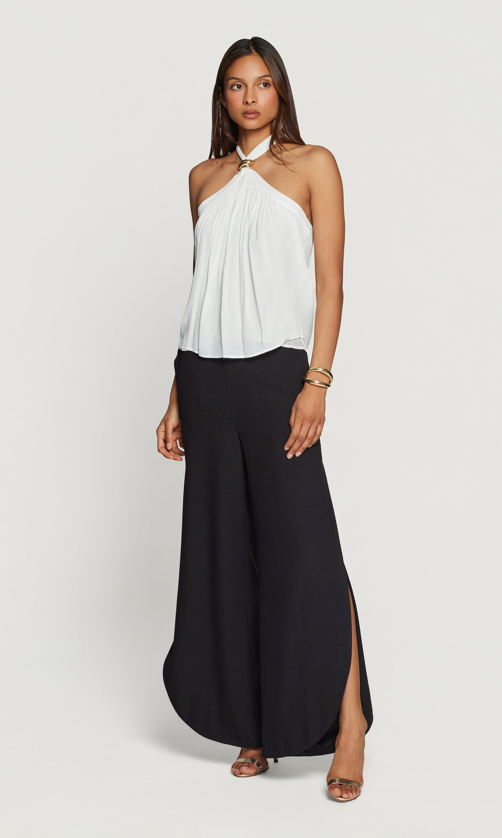 Woman wearing a white halter top and black wide-leg pants on a light gray background