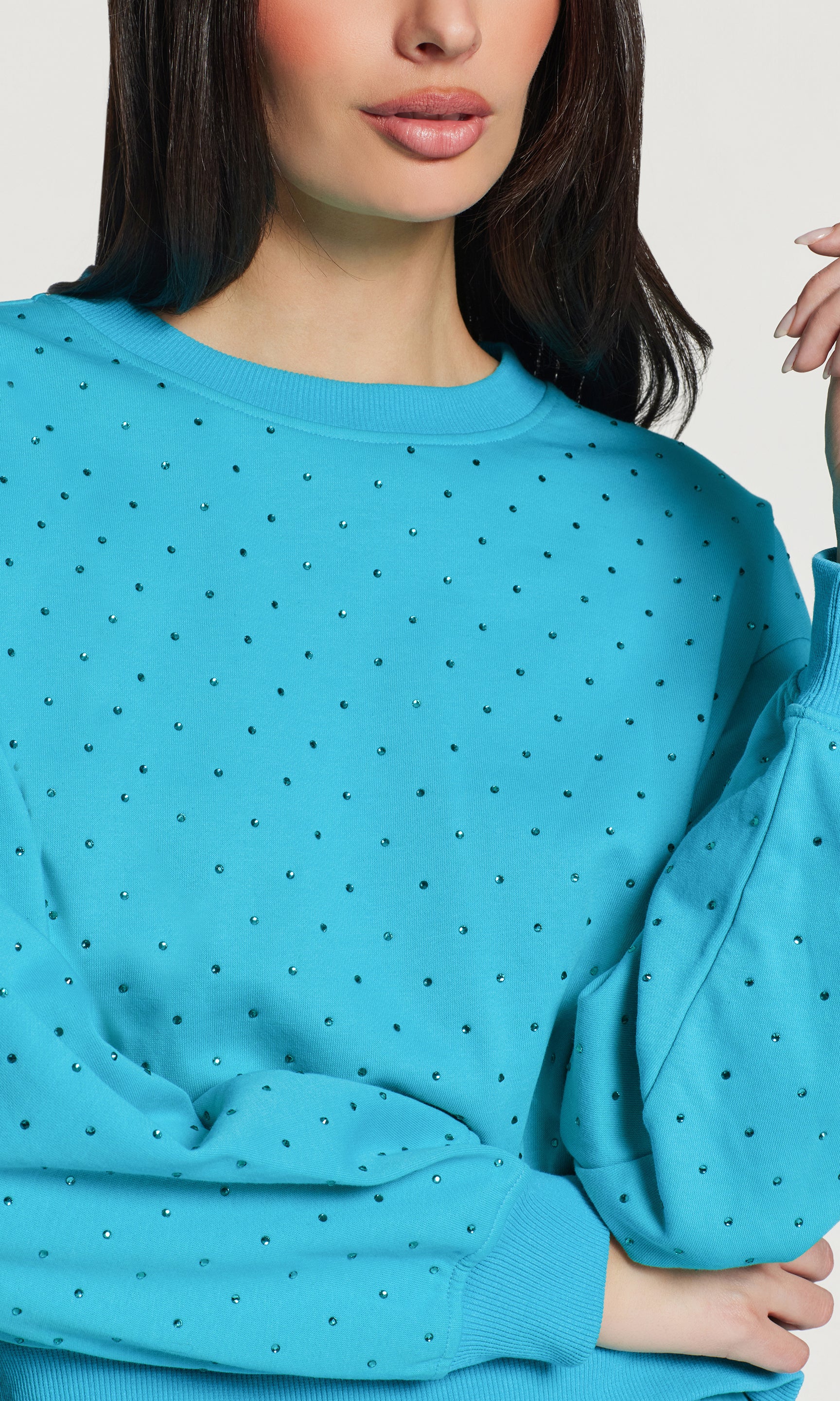 Close-up of blue crystal embellished sweatshirt worn by a person against a neutral background