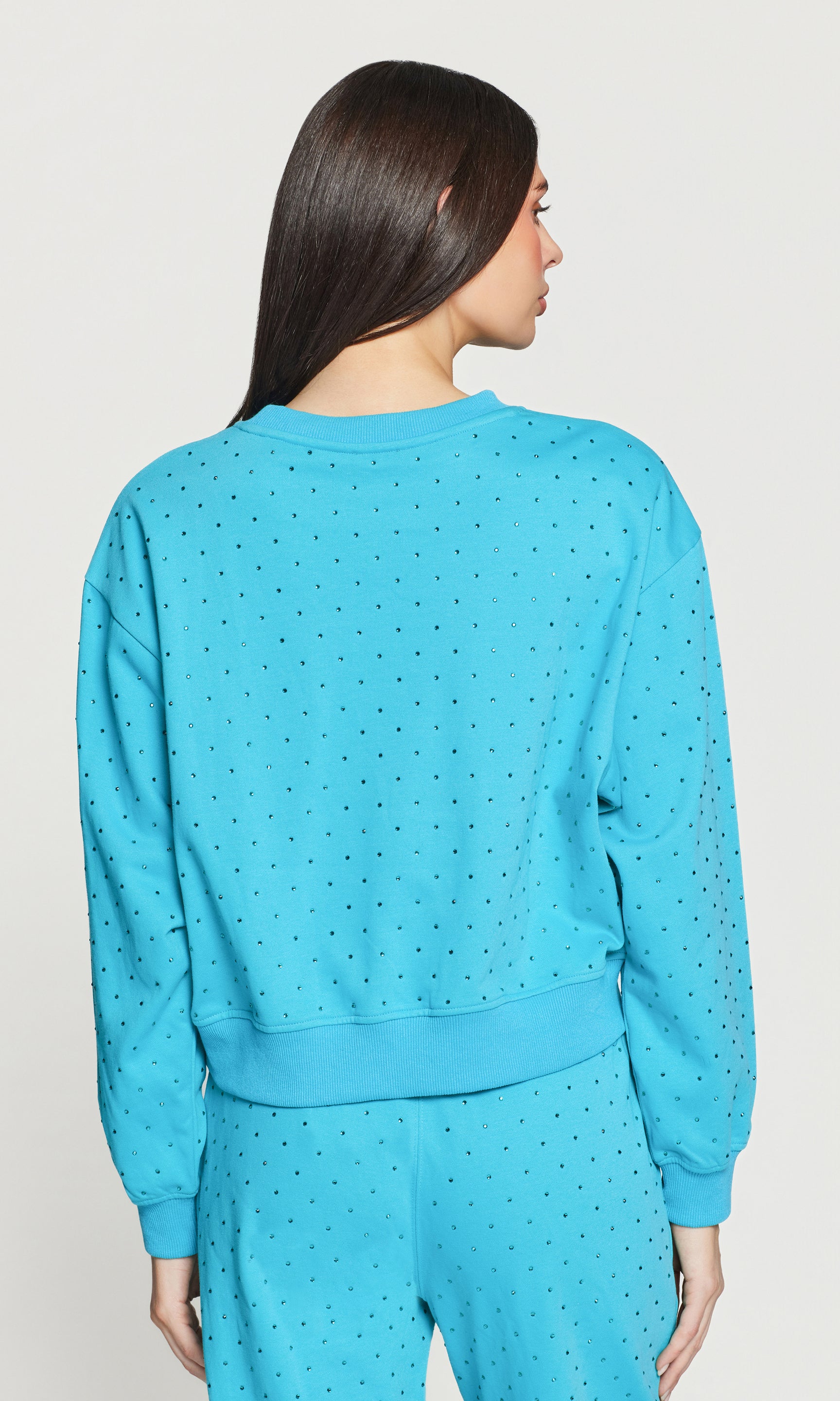 Back view of woman wearing a blue crystal embellished sweater on a light gray background