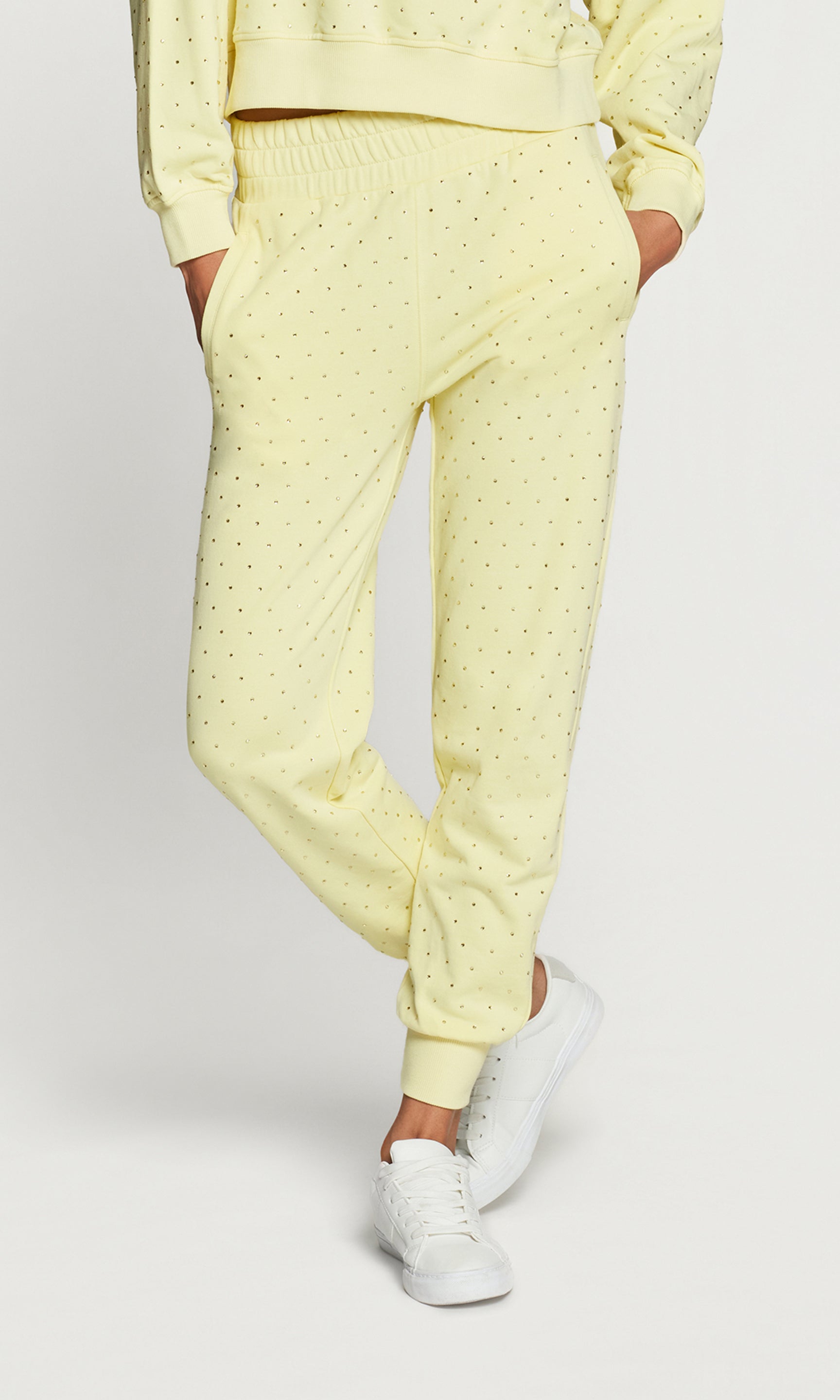 Person wearing a yellow crystal embellished pants with white sneakers on a light gray background