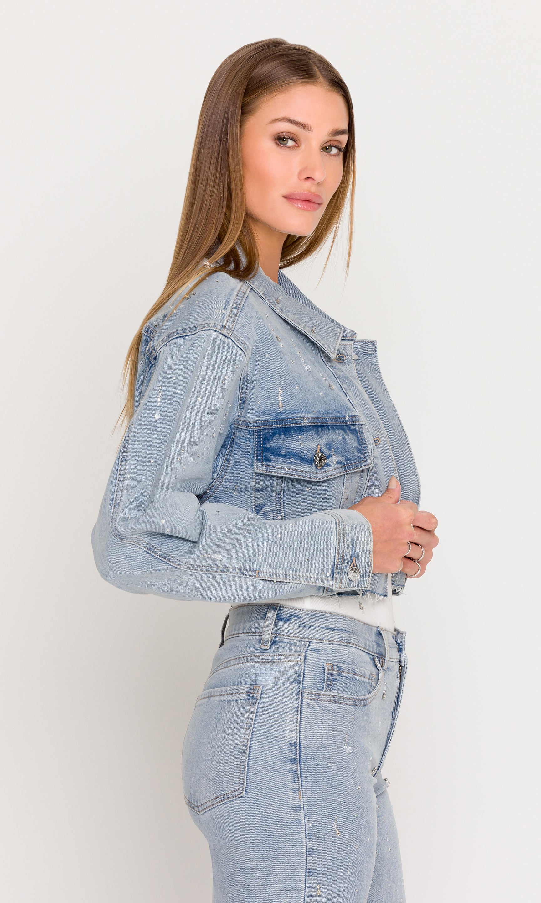 Side view of woman wearing a light blue denim jacket and jeans against a white background