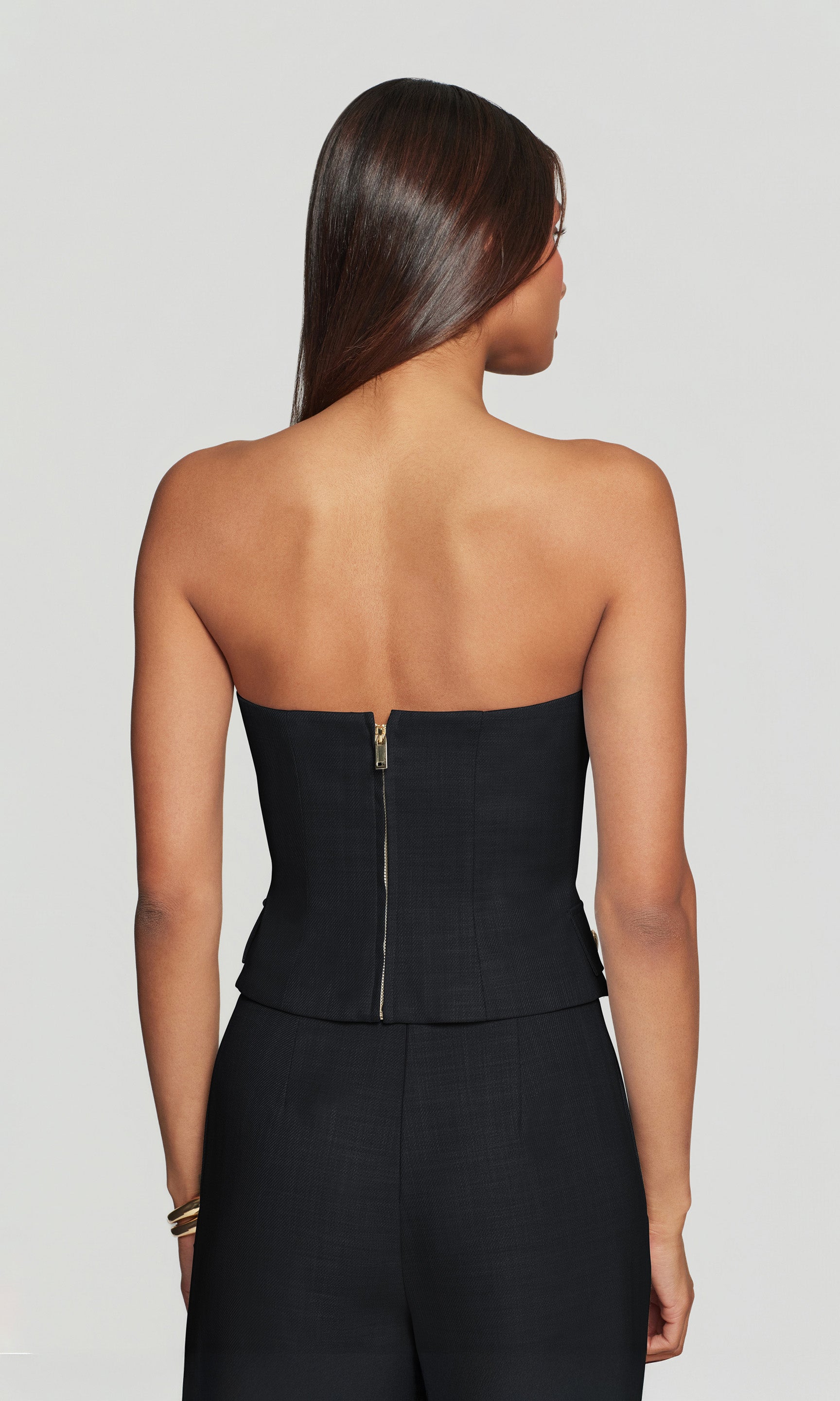 Back view of woman wearing a black strapless top on a plain background
