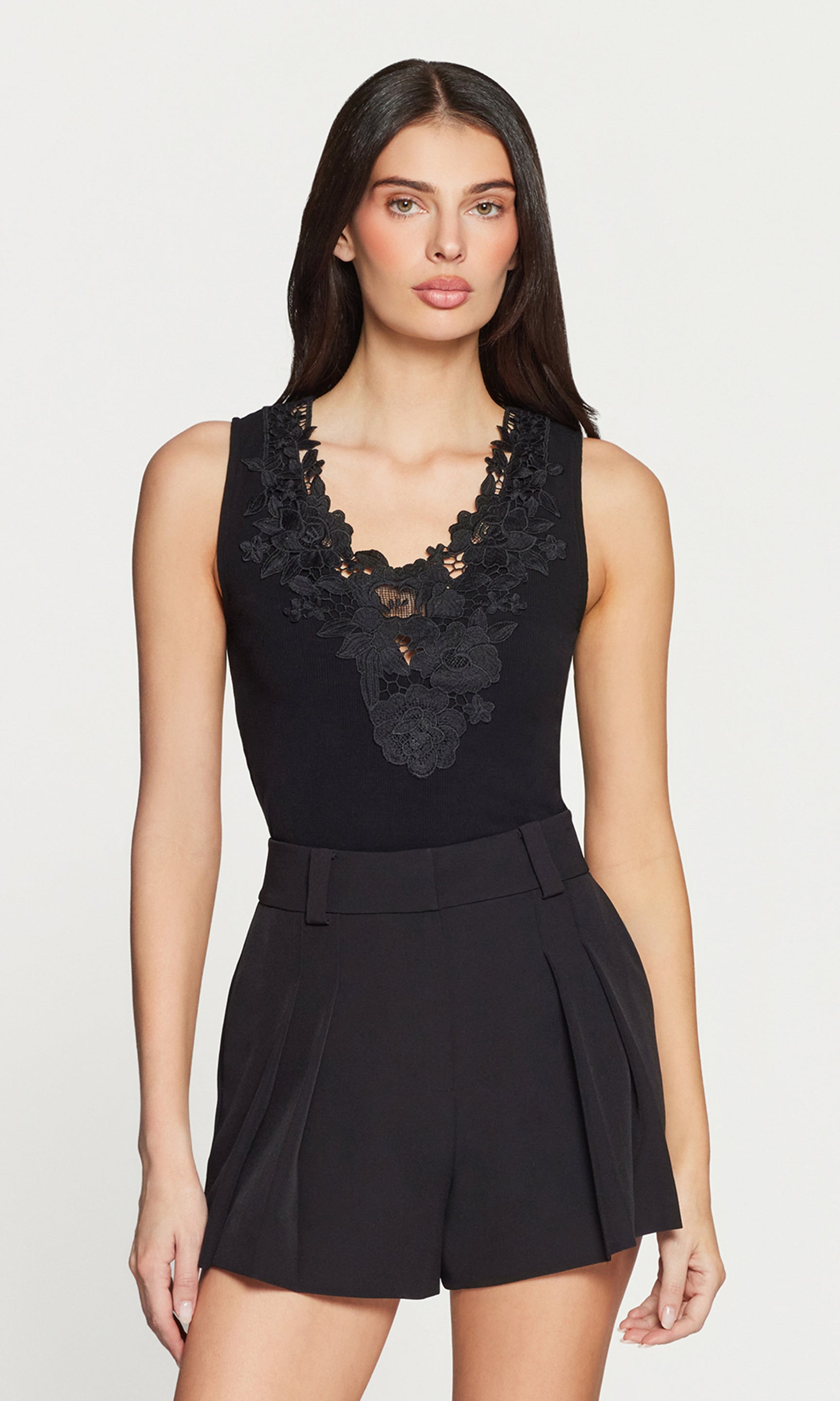 Woman wearing a black sleeveless top with lace details and black shorts on a white background