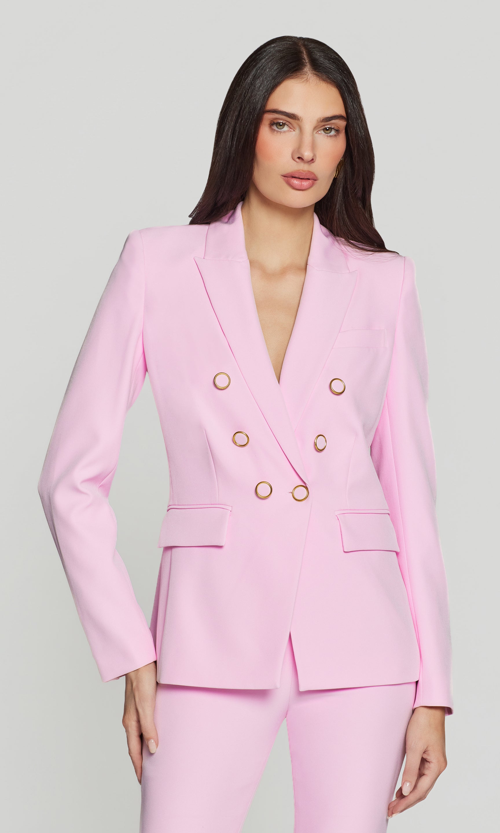Woman wearing a pink suit with gold buttons on a light gray background