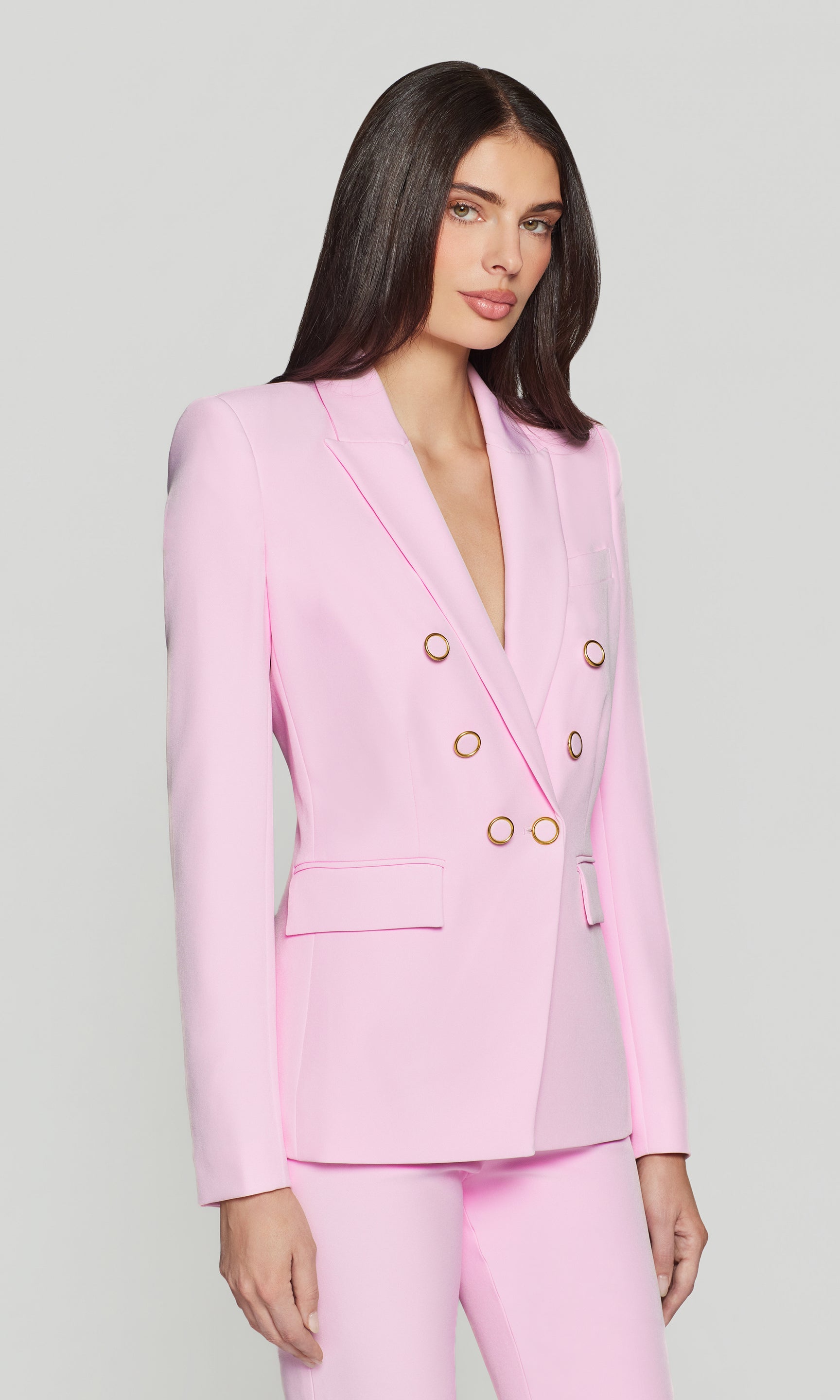 Side view of woman wearing a pink suit with gold buttons on a light gray background