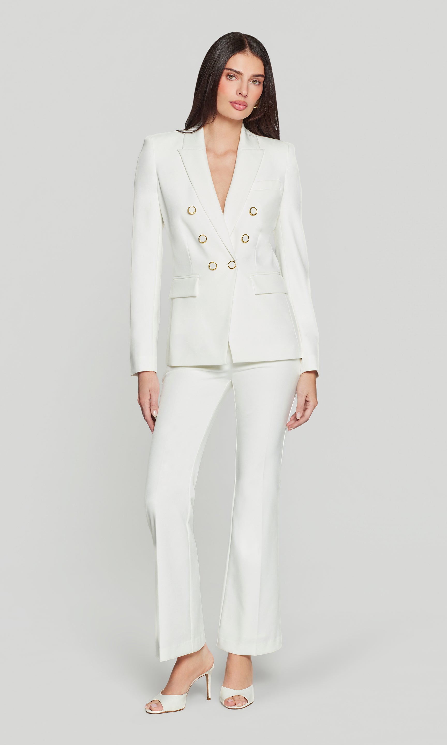 Woman wearing a white suit with gold buttons on a light gray background