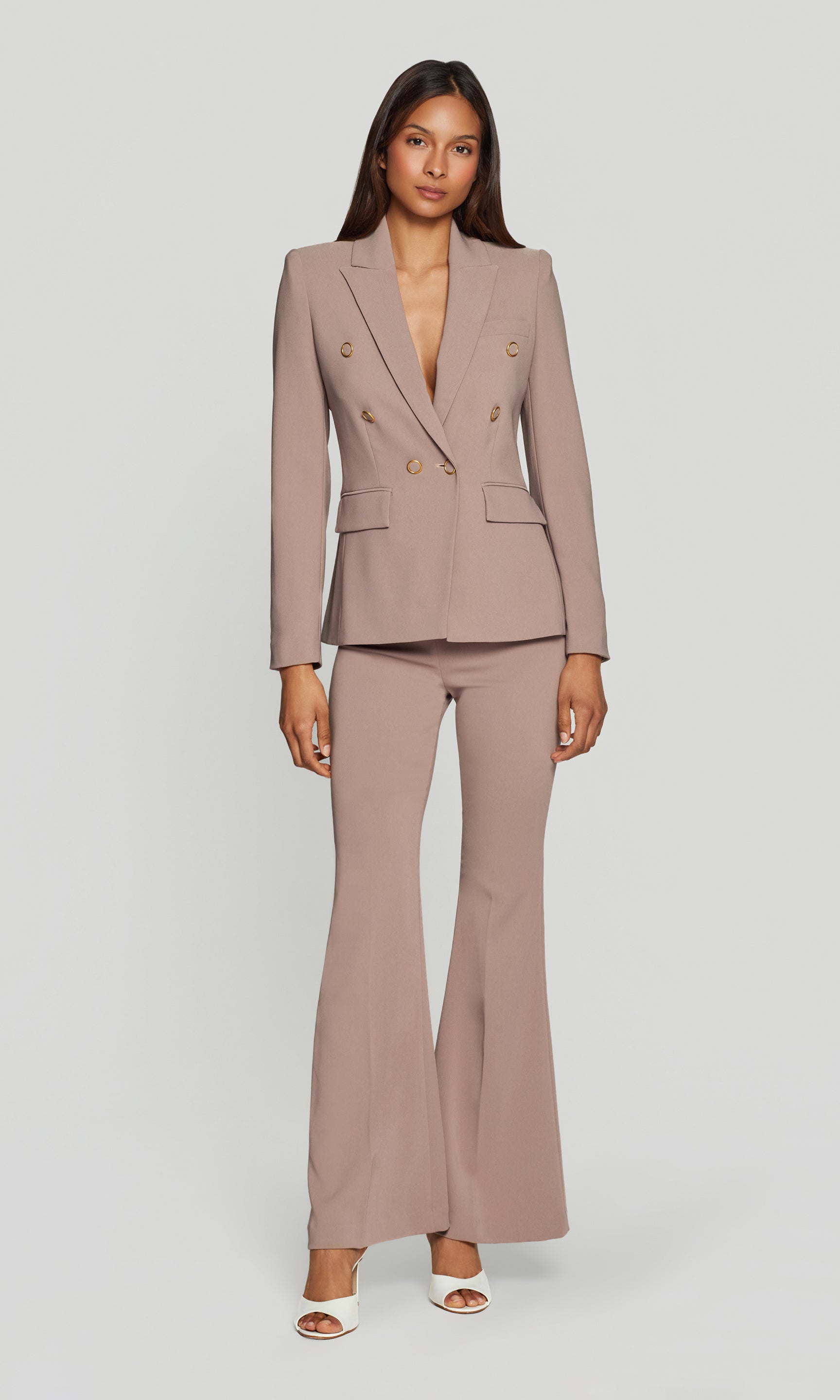 Woman wearing a matching beige suit with a blazer and flared pants on a plain background