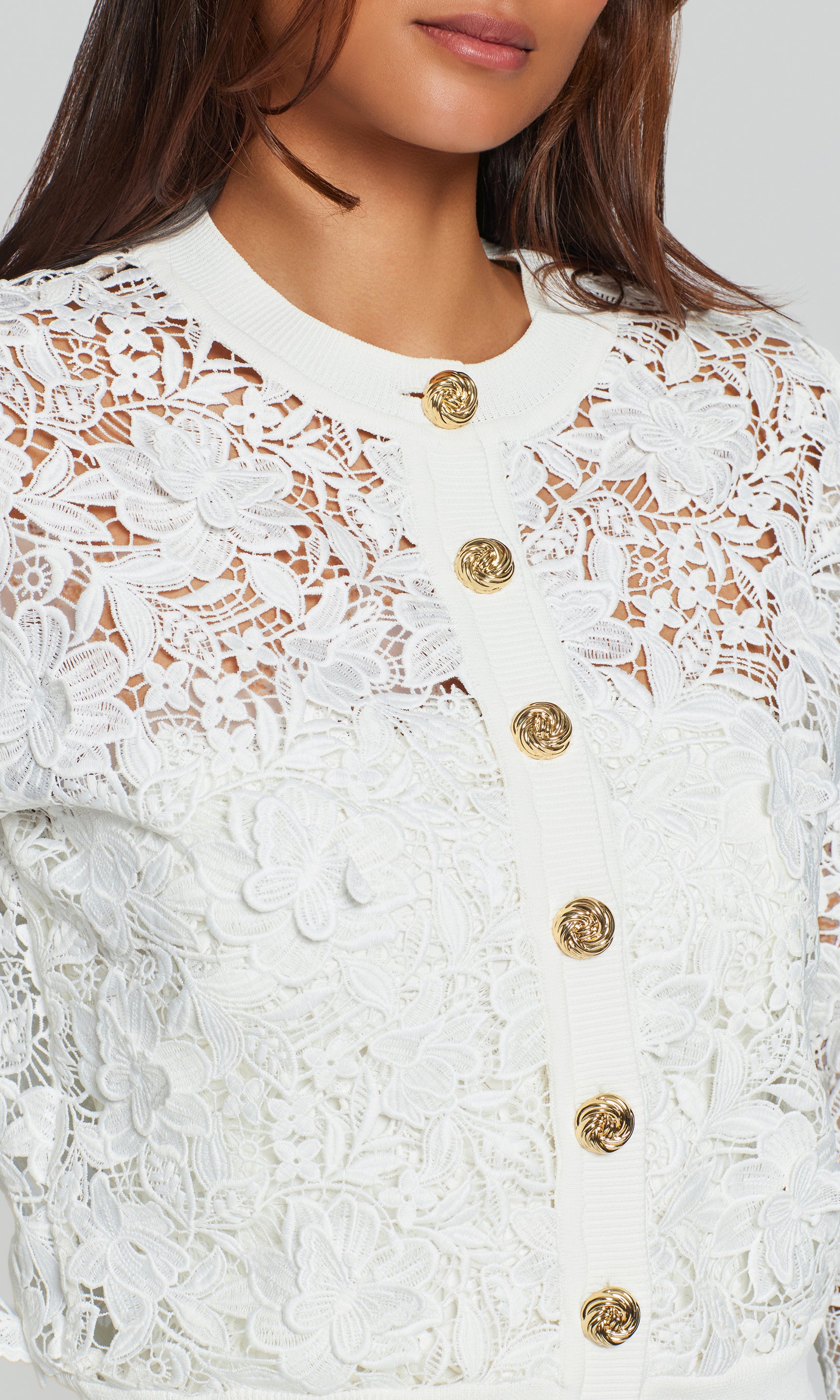 Close-up of white lace garment with gold buttons on a white background
