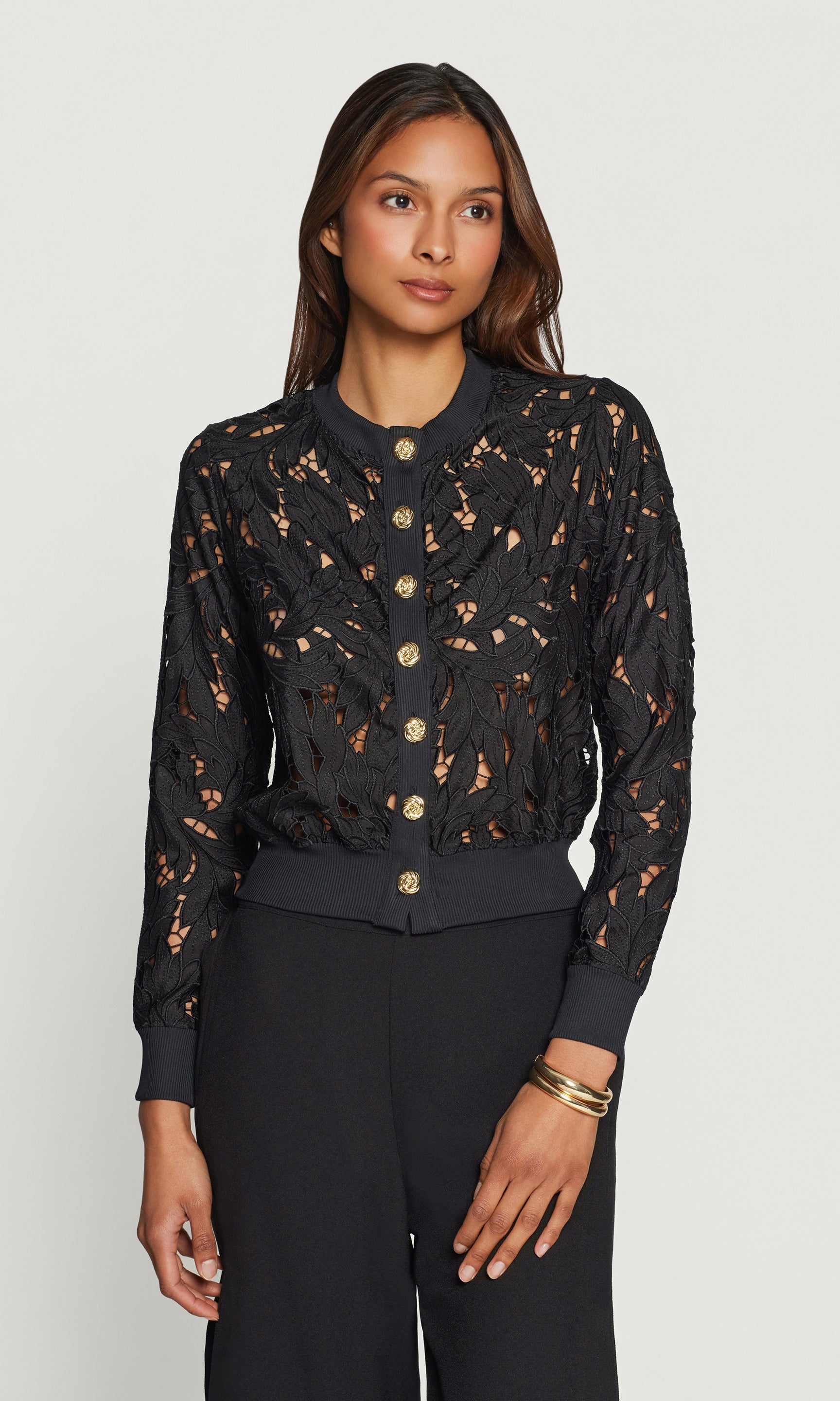 Woman wearing a black lace cardigan with gold buttons on a white background