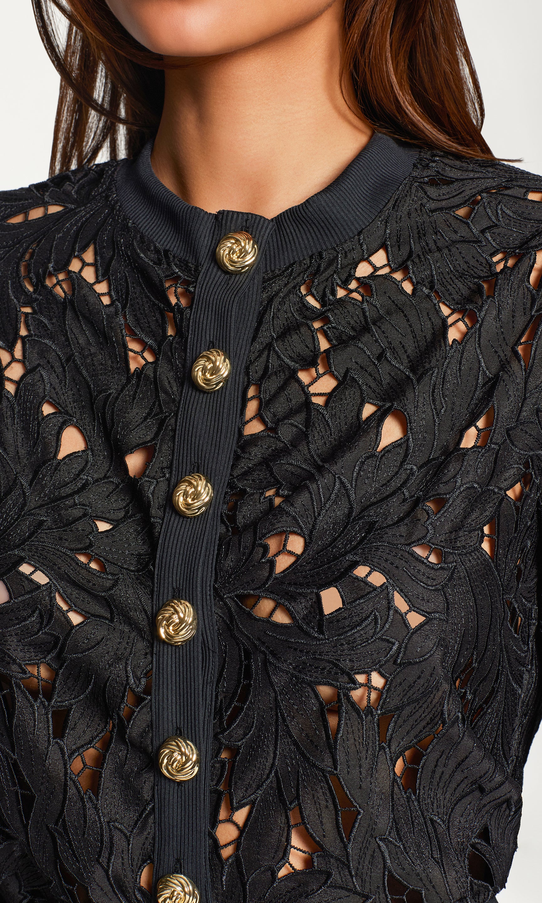 Close-up of black lace cardigan with gold buttons on a neutral background