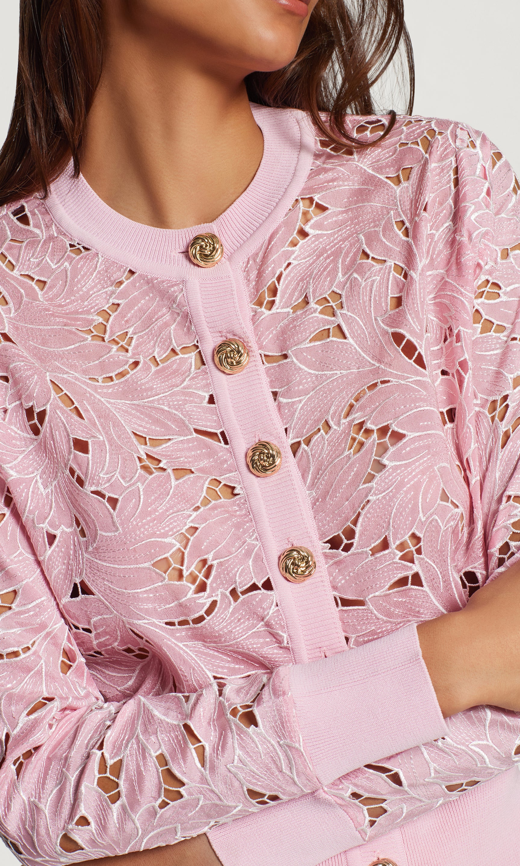 Close-up of a pink lace cardigan with gold buttons on a white background