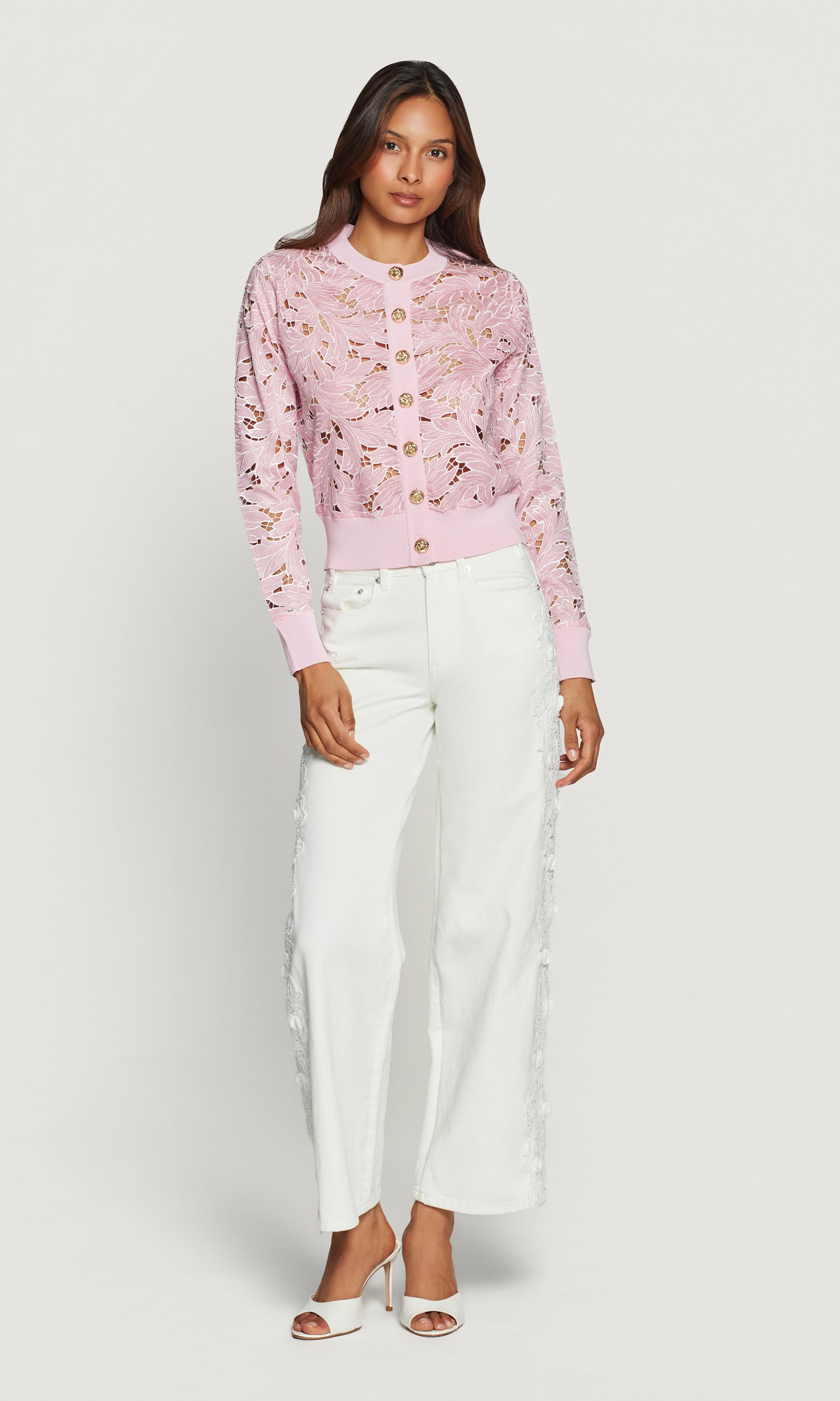 Woman wearing a pink floral cardigan and white pants on a white background
