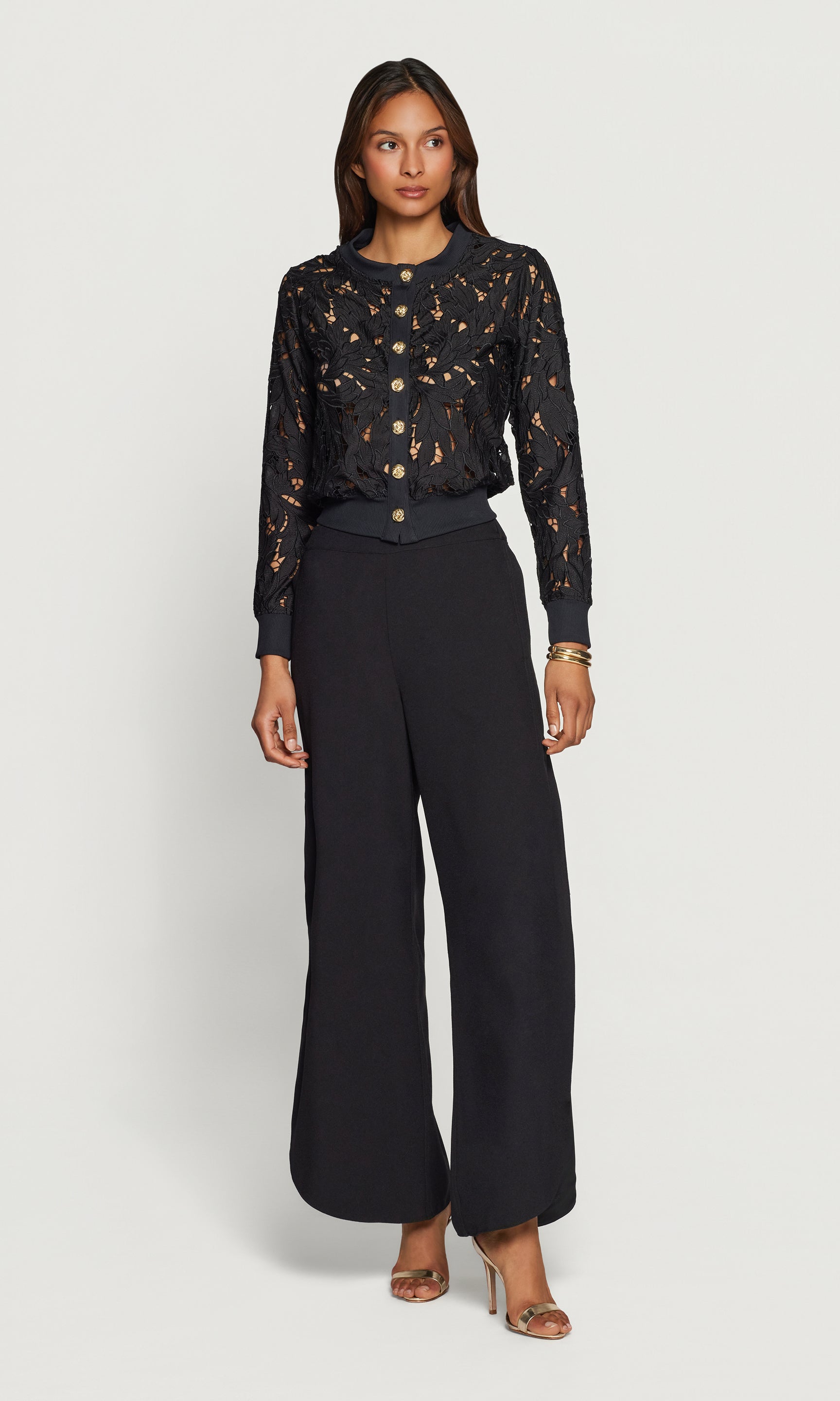 Woman wearing a black lace cardigan and wide-leg pants on a white background