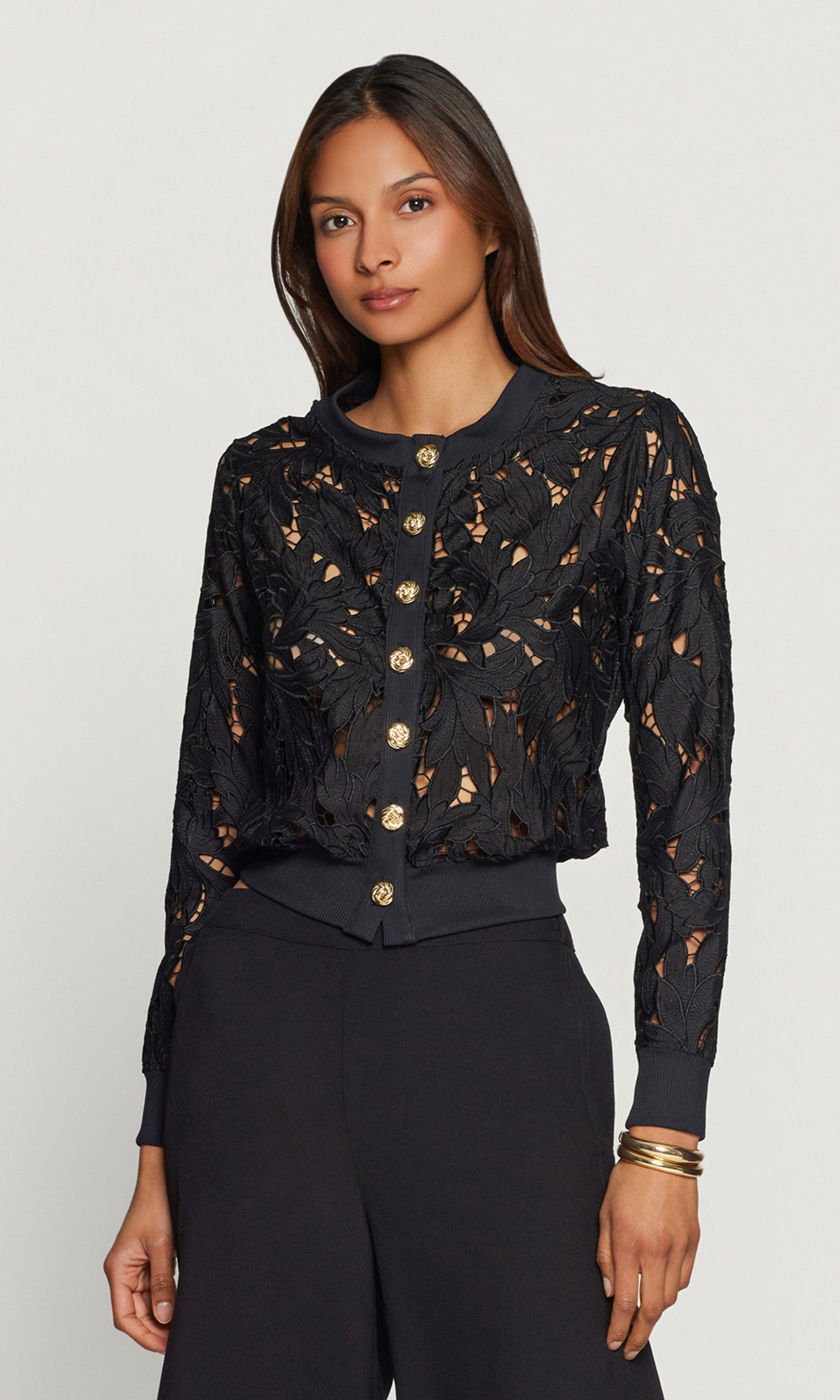 Woman wearing a black lace top with gold buttons on a white background