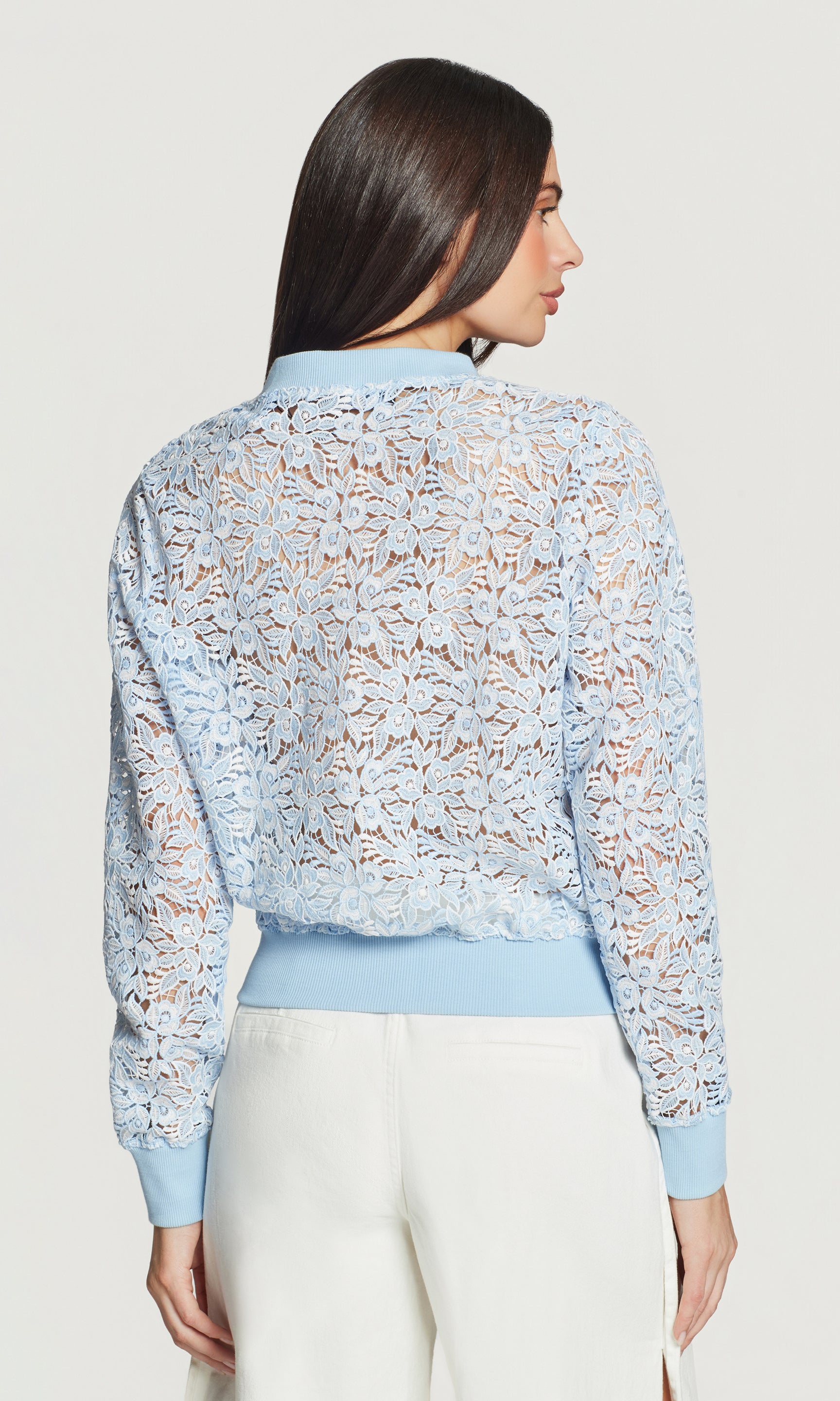 Back view of woman wearing a light blue floral lace top with a plain background