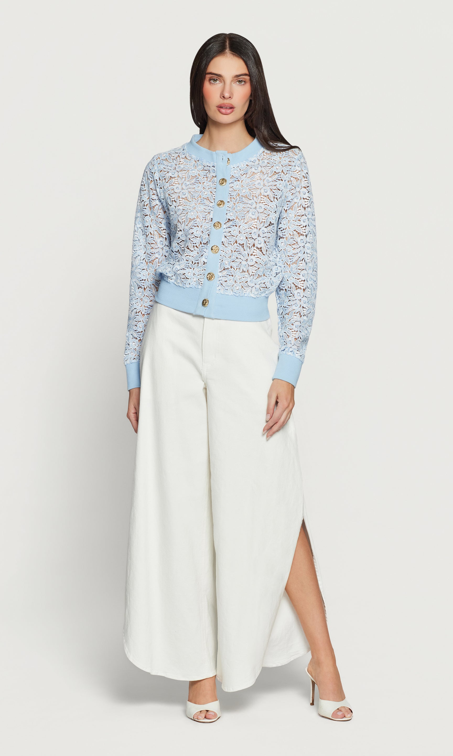 Woman wearing a light blue floral cardigan with white jeans on a white background