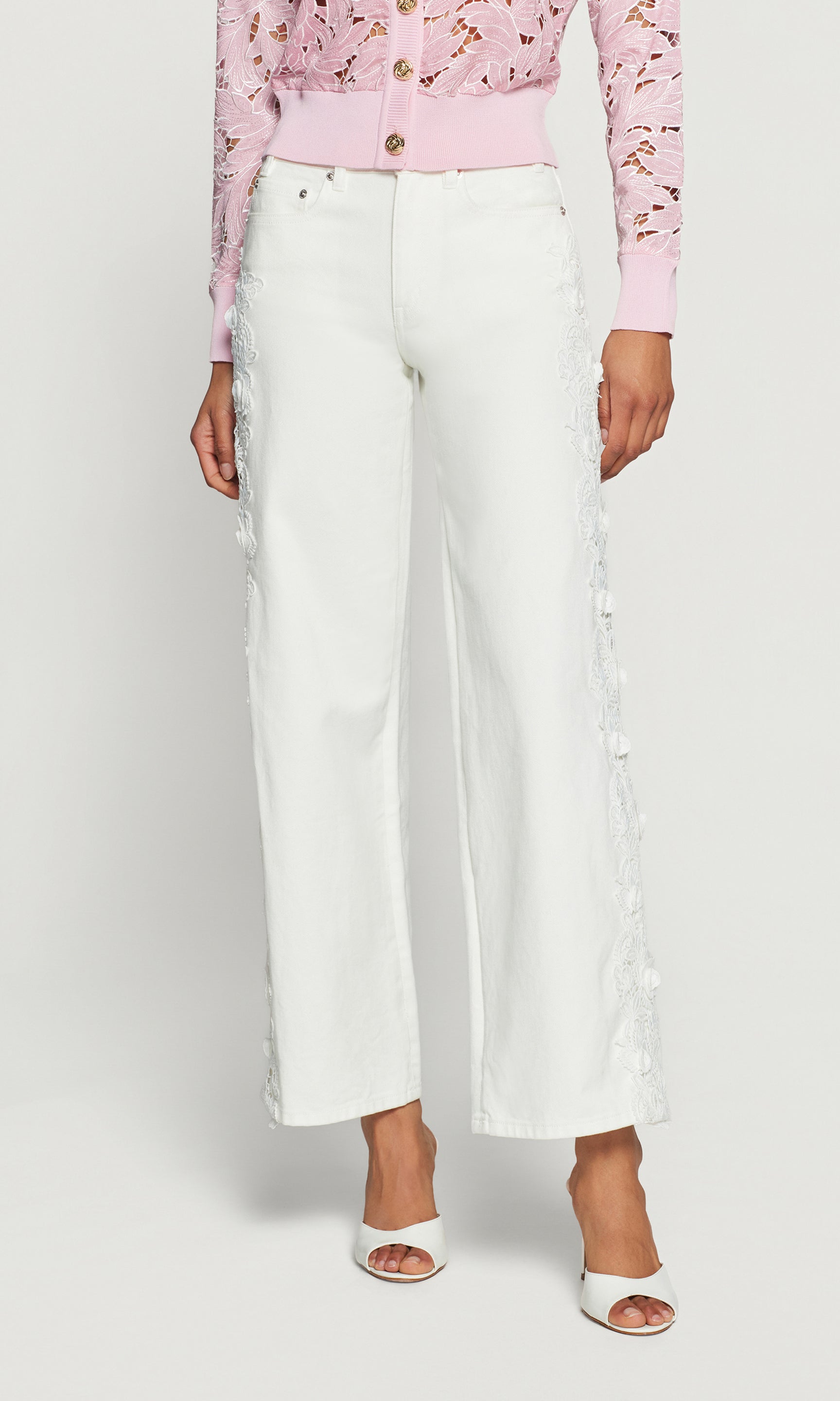 Person wearing a pink floral blouse and white pants on a plain background