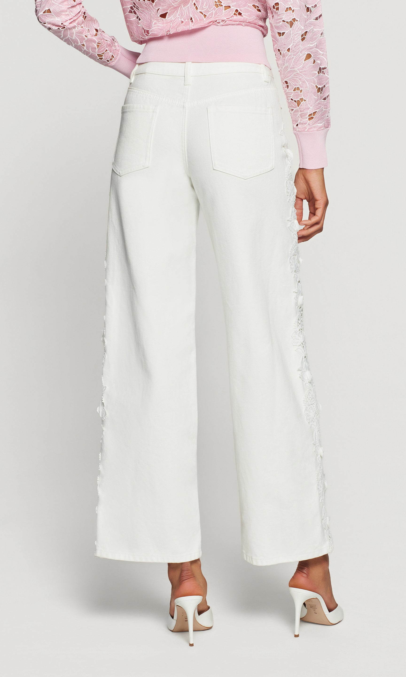 Back view of white wide-leg pants worn with a pink top on a plain background