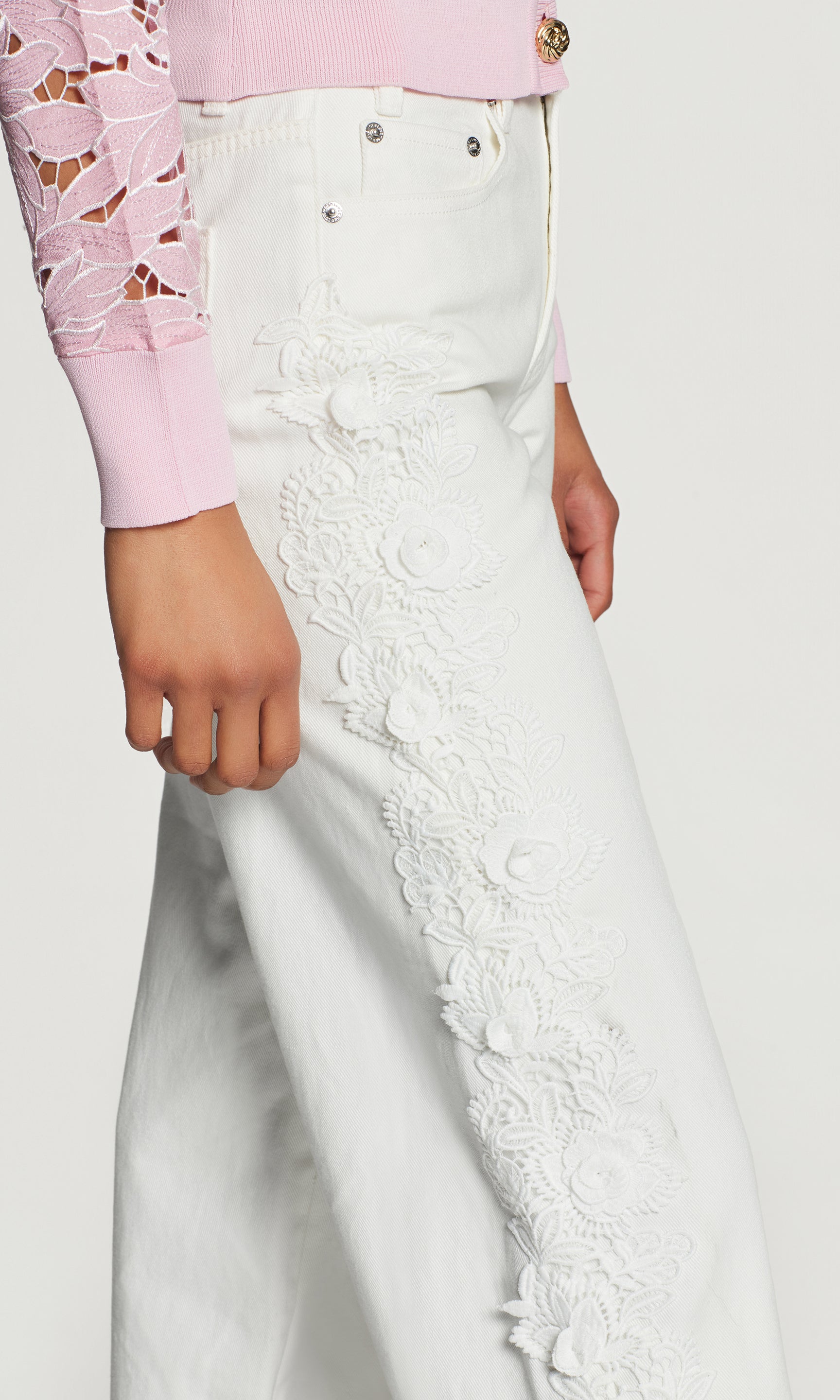 Close-up of white lace pants worn with a pink top on a plain background