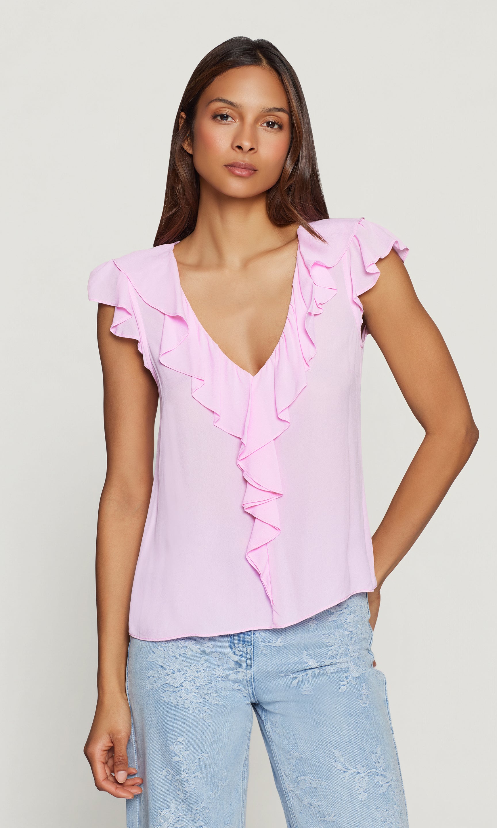 Woman wearing a pink ruffled blouse and light blue jeans on a plain background