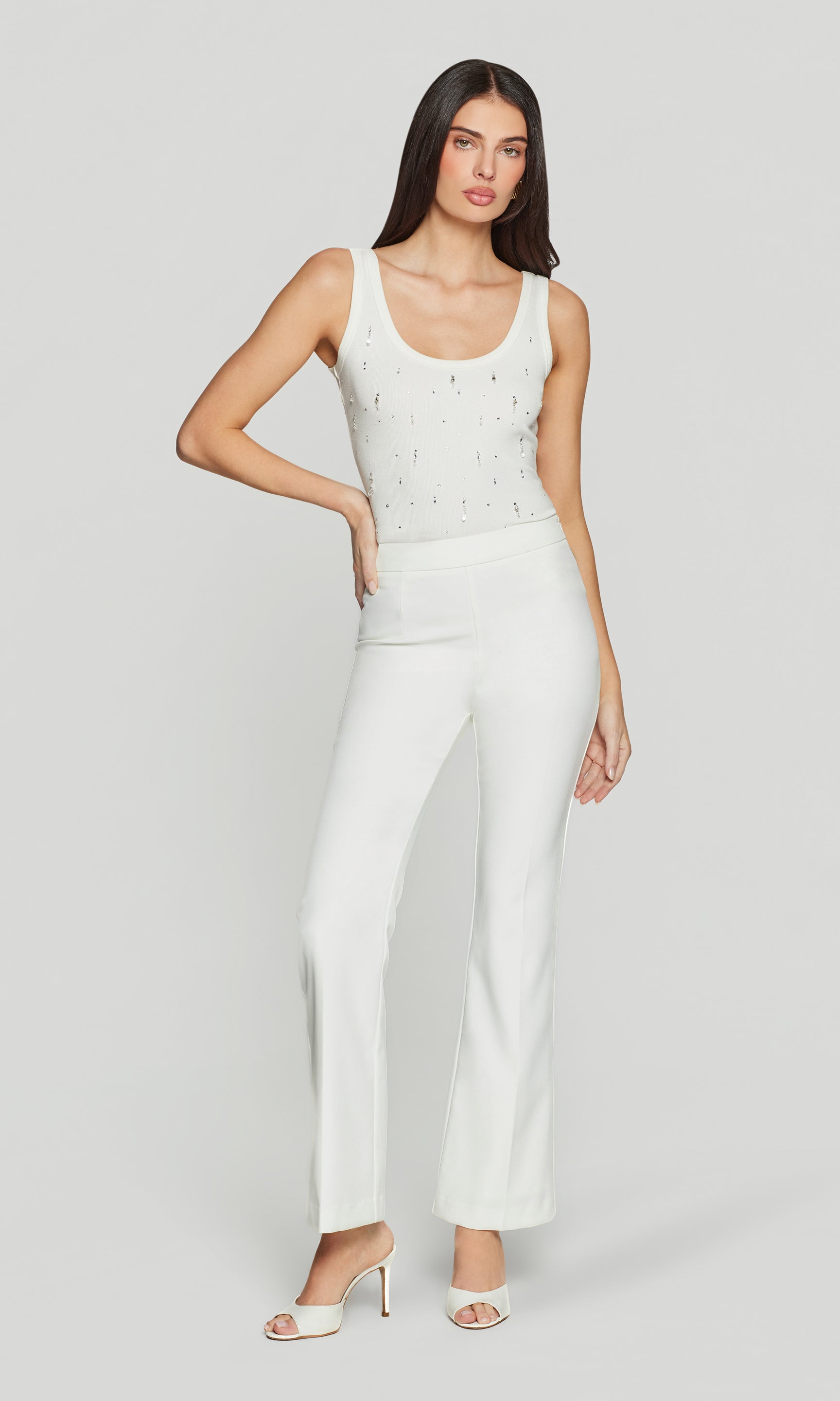 Woman wearing a white tank and trousers with a plain background