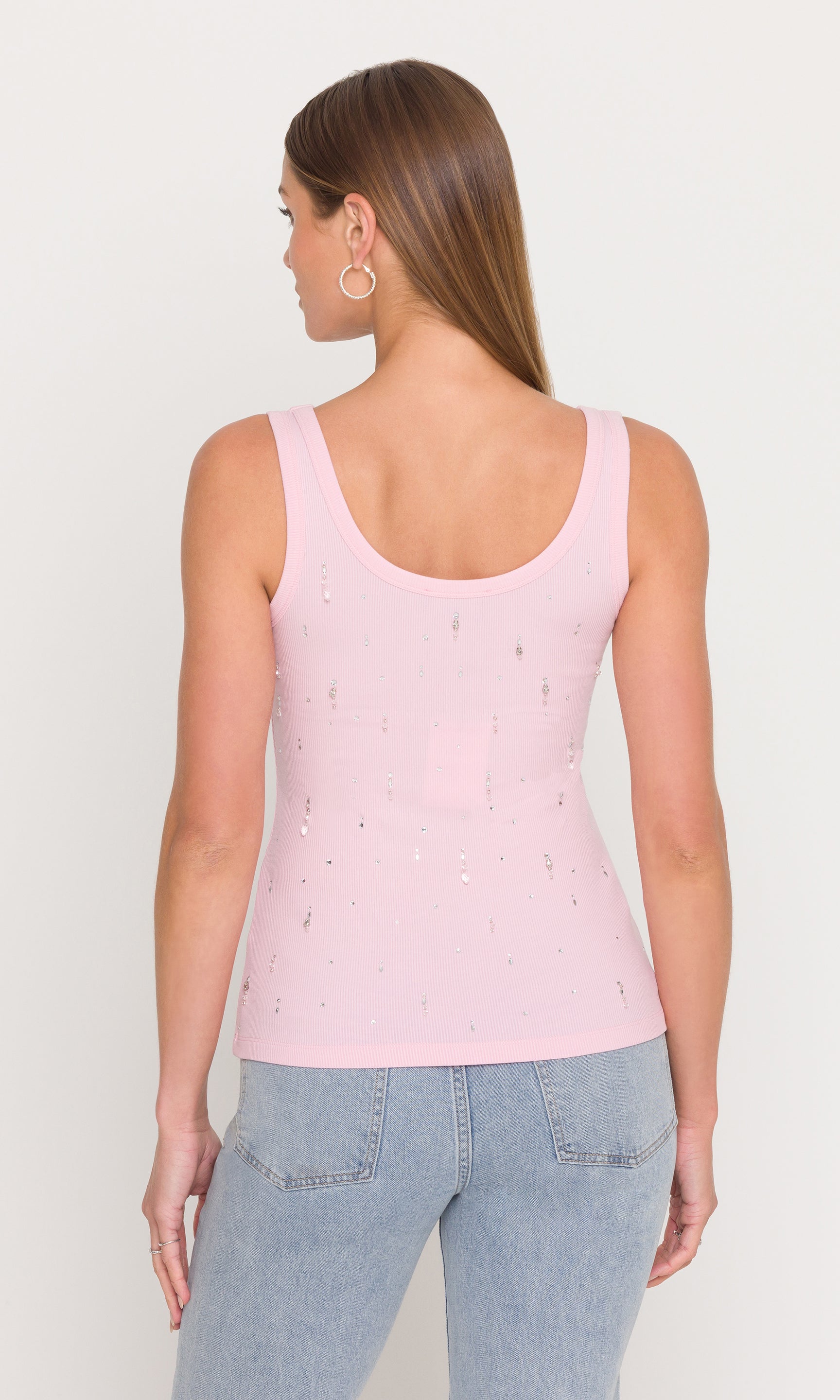 In a rear view, the model wears the Evita Embellished Top in pink with denim, showing the smooth back and classic tank silhouette.