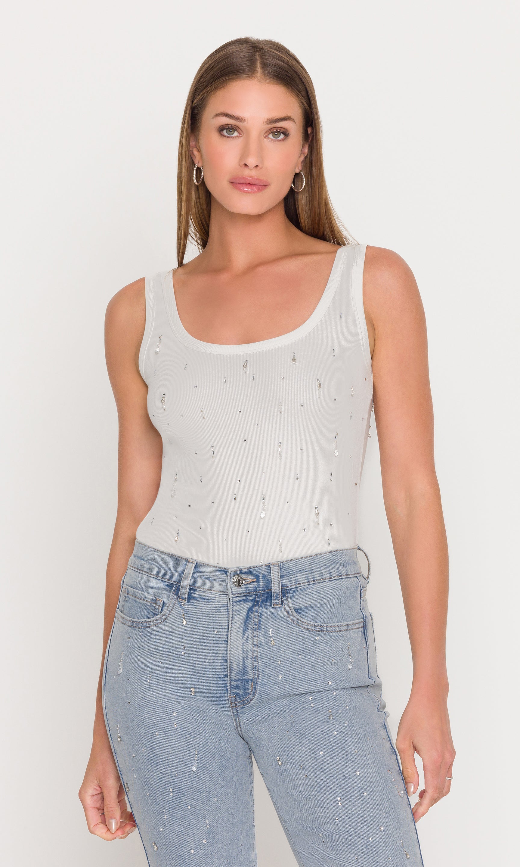 The model is shown in a three-quarter front view wearing the Evita Embellished Top in white with denim, emphasizing the classic tank shape and refined sparkle.