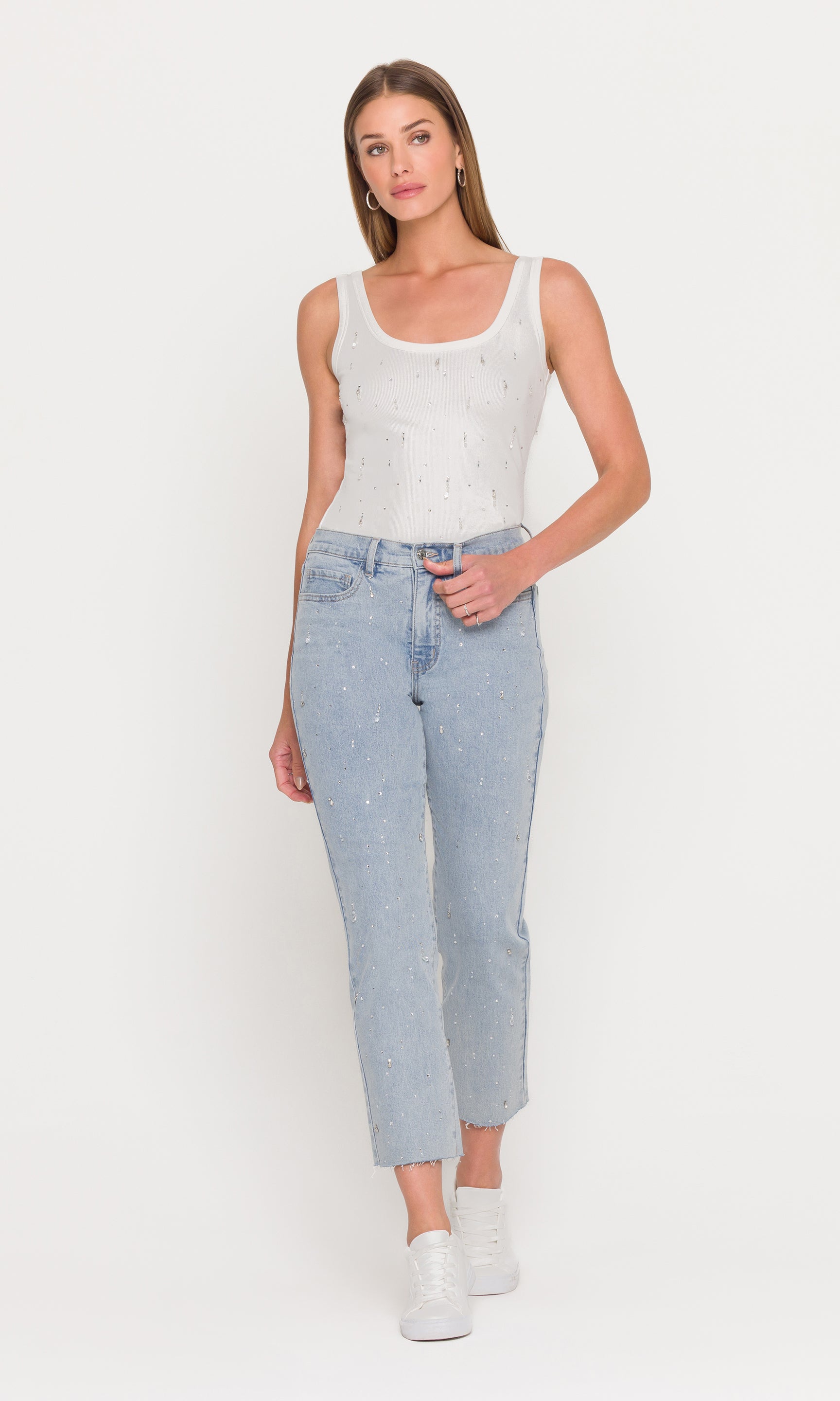 The model appears in a full body front view wearing the Evita Embellished Top in white with light wash jeans, showcasing the sleek, body-skimming fit and embellished finish.
