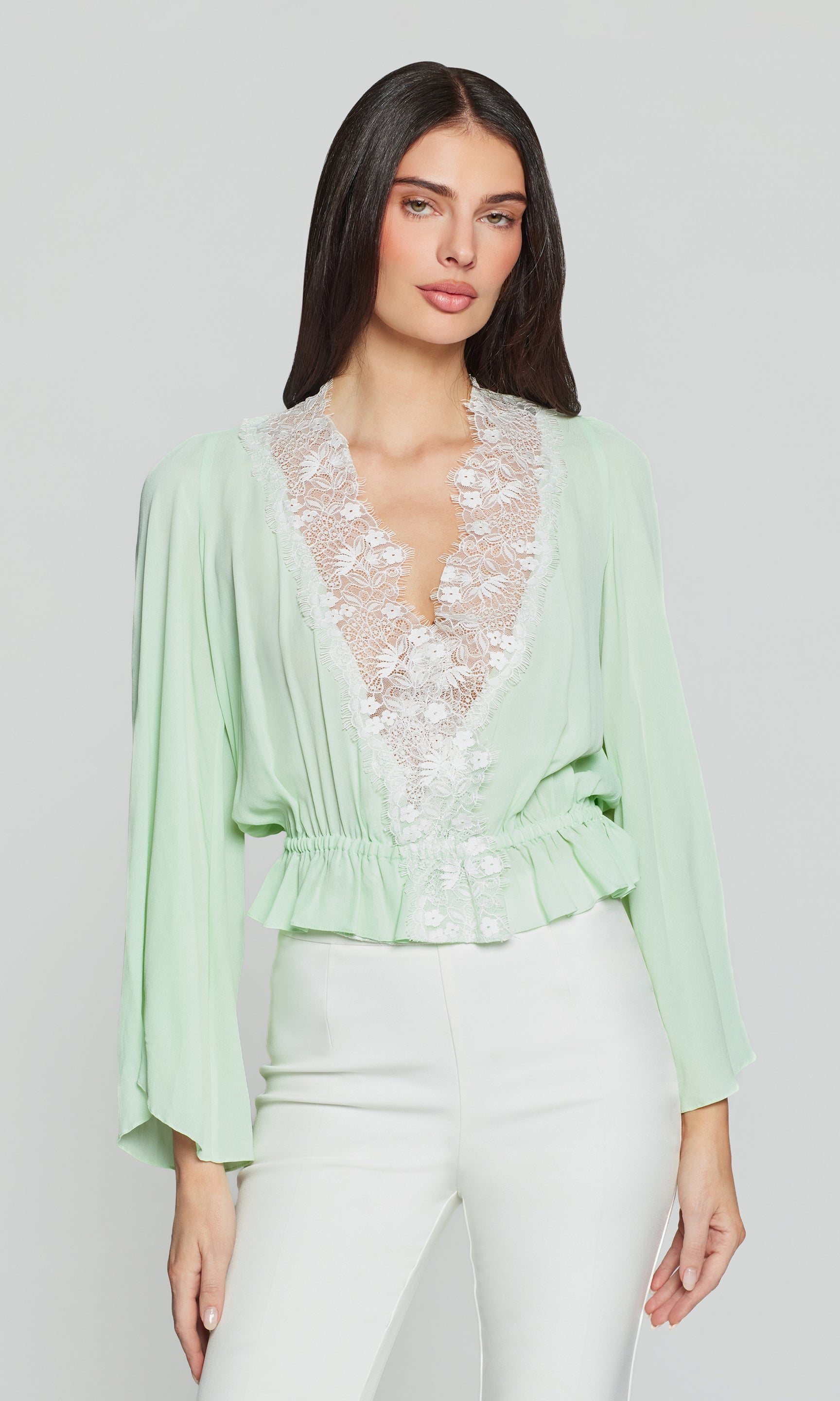 Woman wearing a light green blouse with lace details on a white background