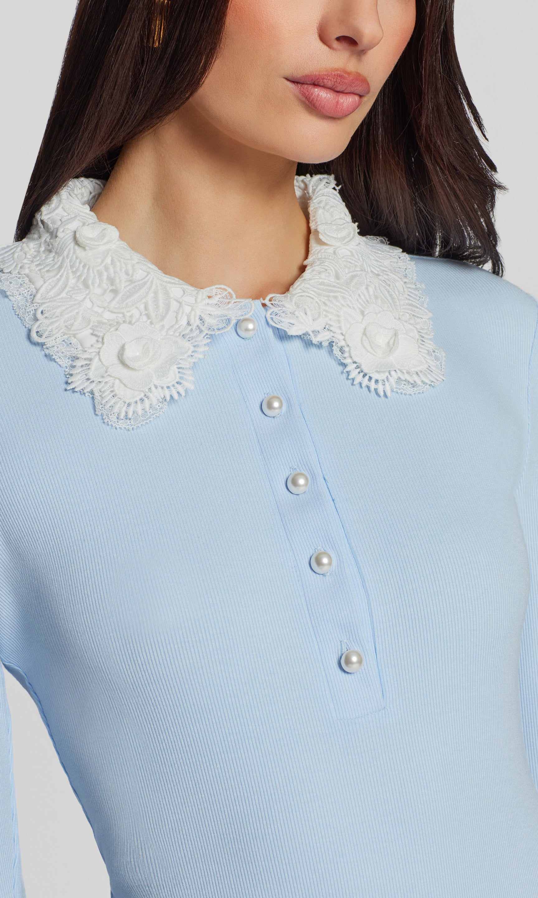 Close-up of light blue top with white lace collar and pearl buttons on a neutral background