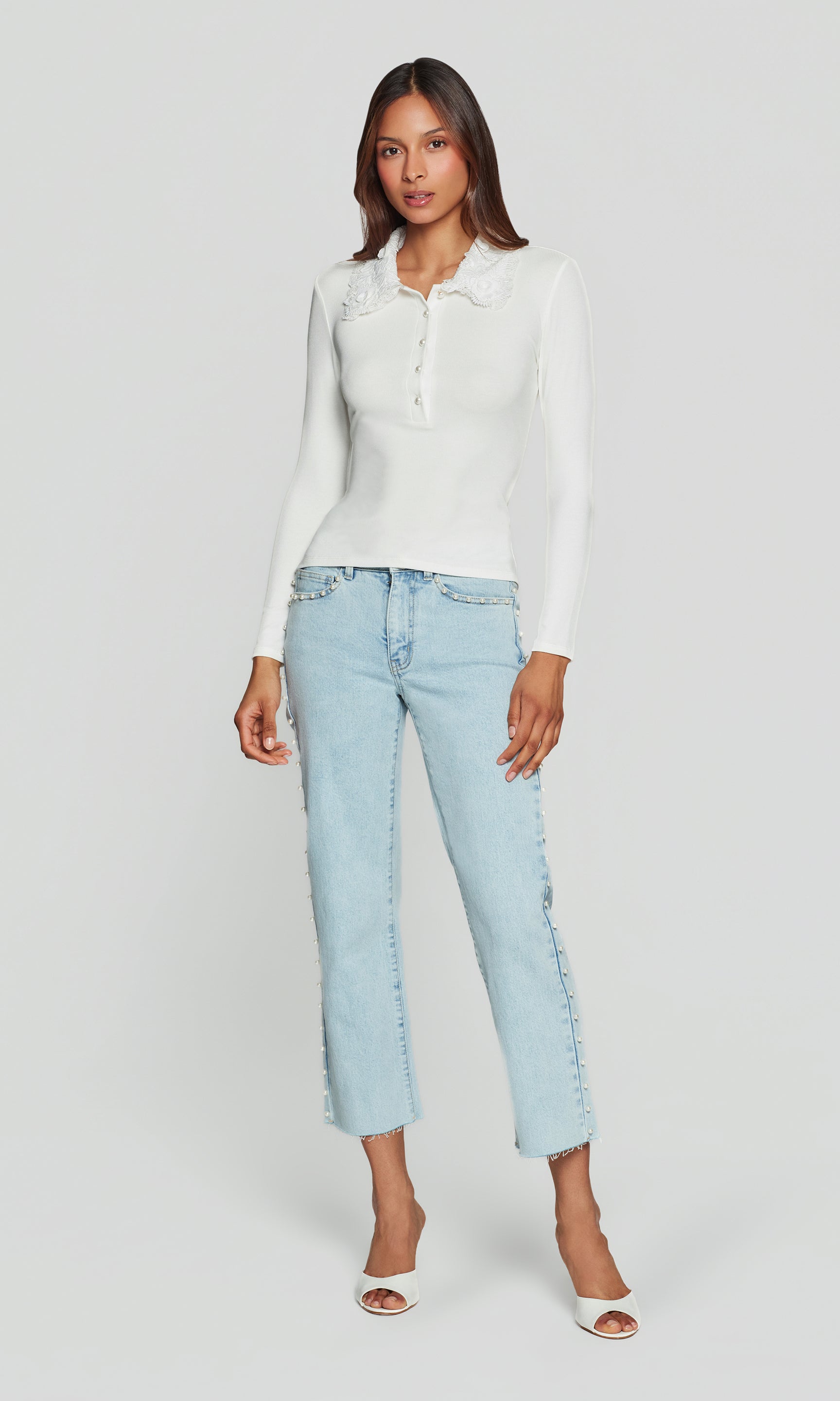 Woman wearing a white sweater and light blue jeans on a plain background