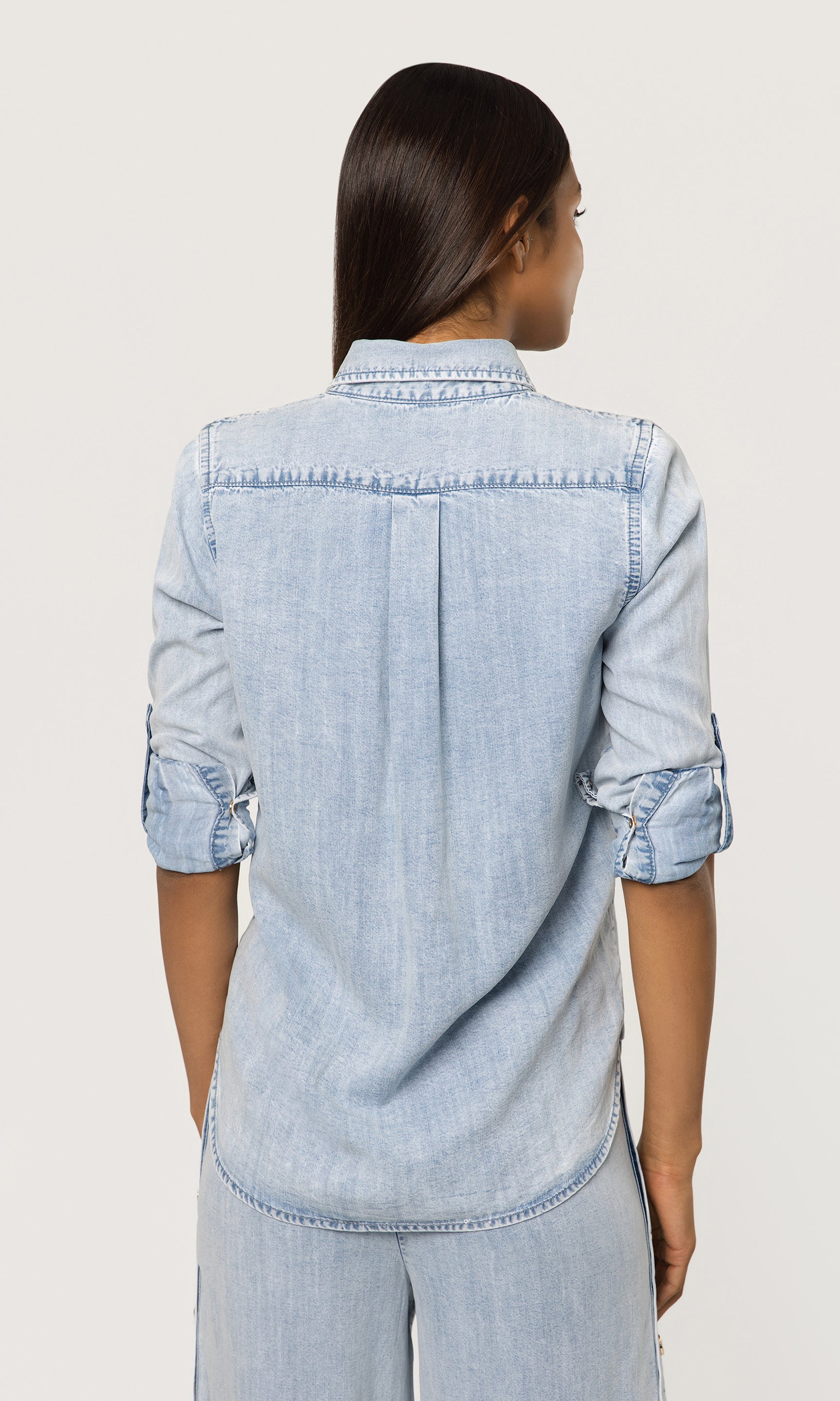 Person wearing a light blue denim shirt on a plain background