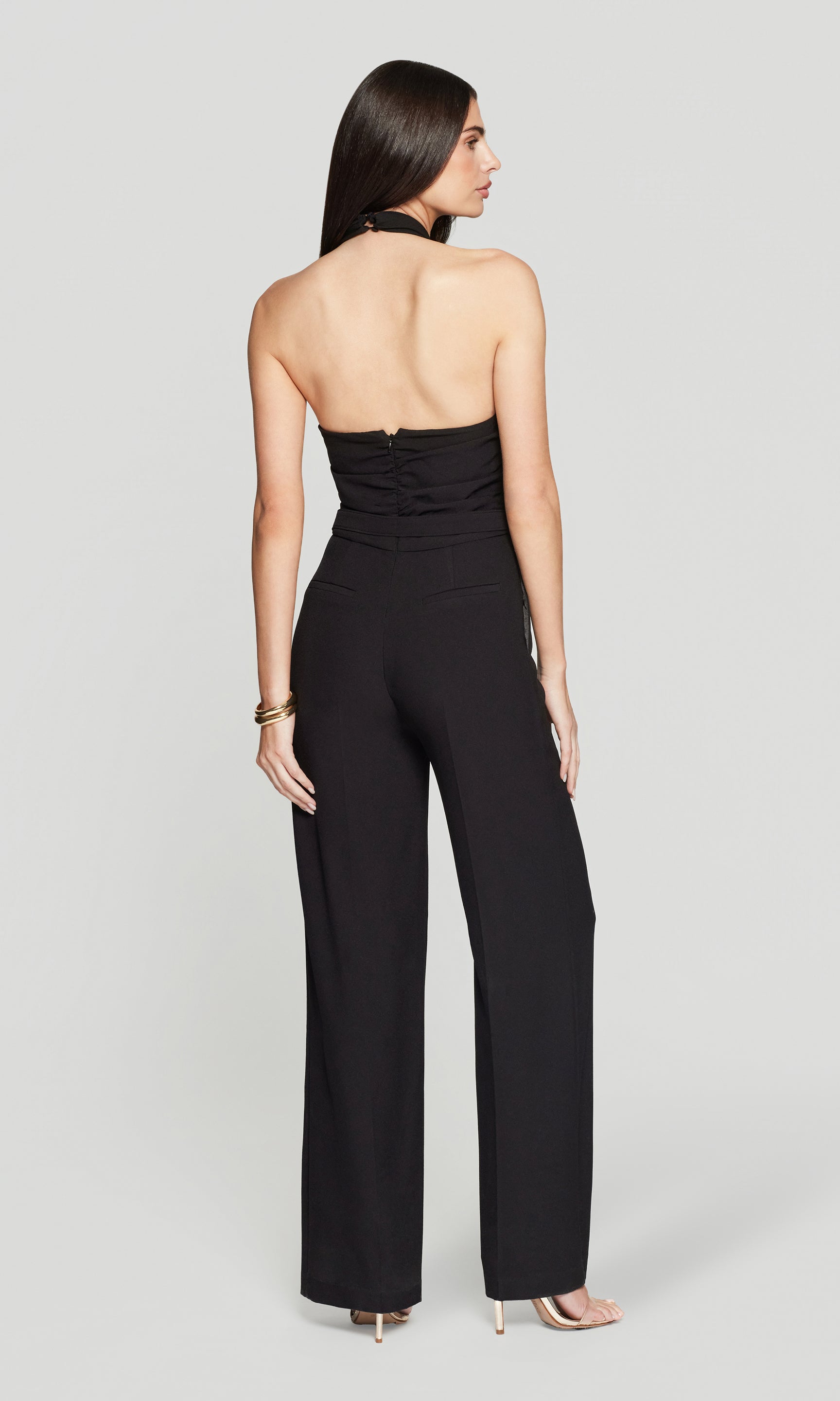 Back view of woman wearing a black strapless jumpsuit on a gray background