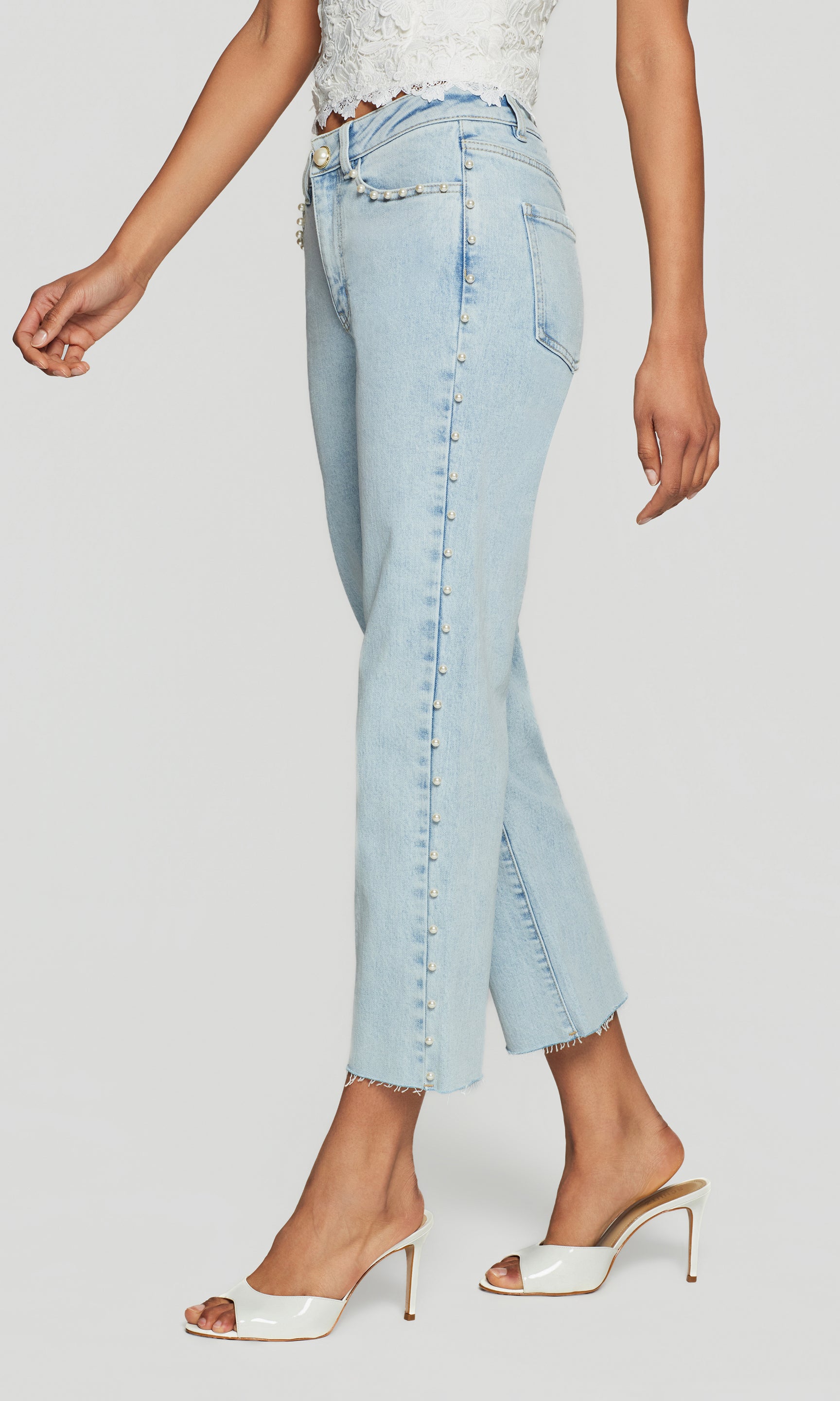 Side view of light blue jeans with pearl embellishments down the side worn by a person on a white background