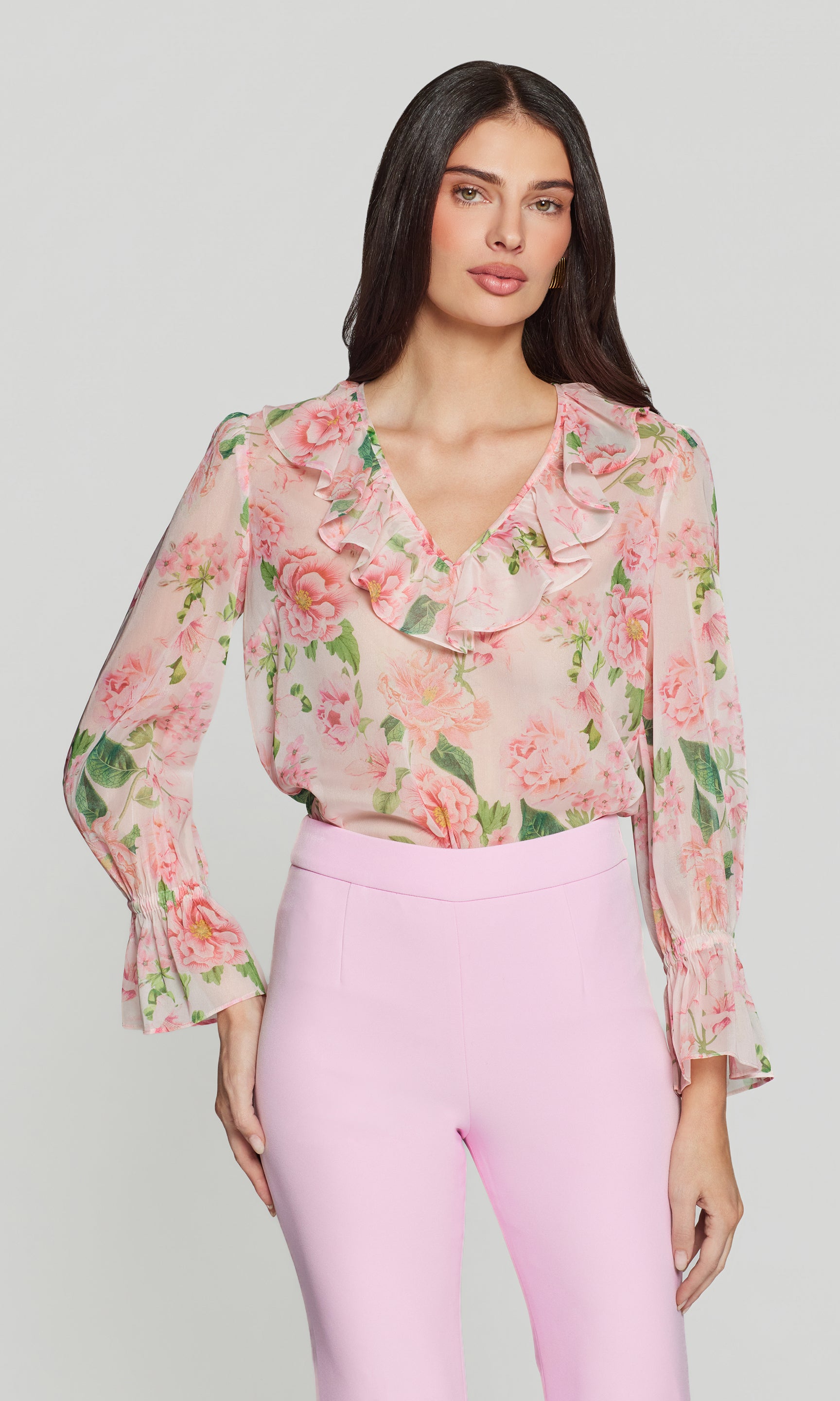Woman wearing a floral blouse and pink pants on a plain background
