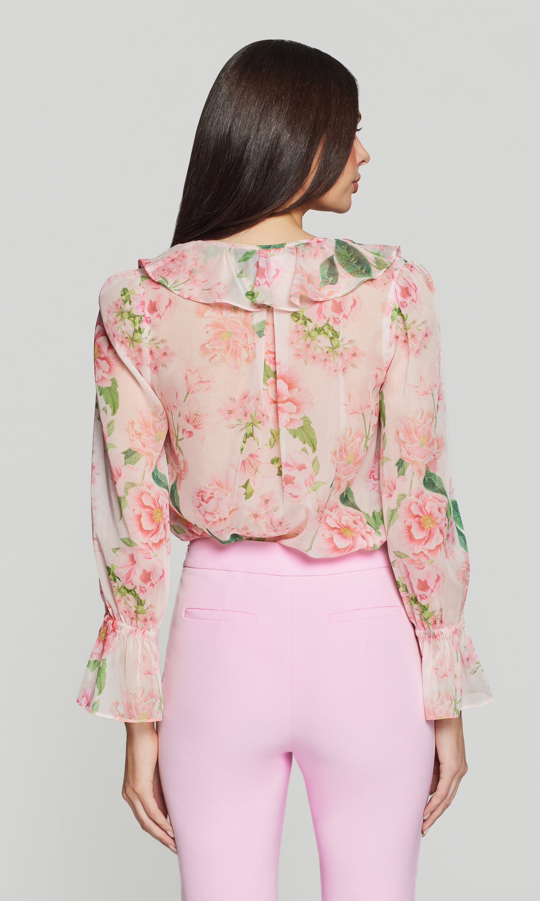 Back view of woman wearing a floral blouse and pink pants against a plain background
