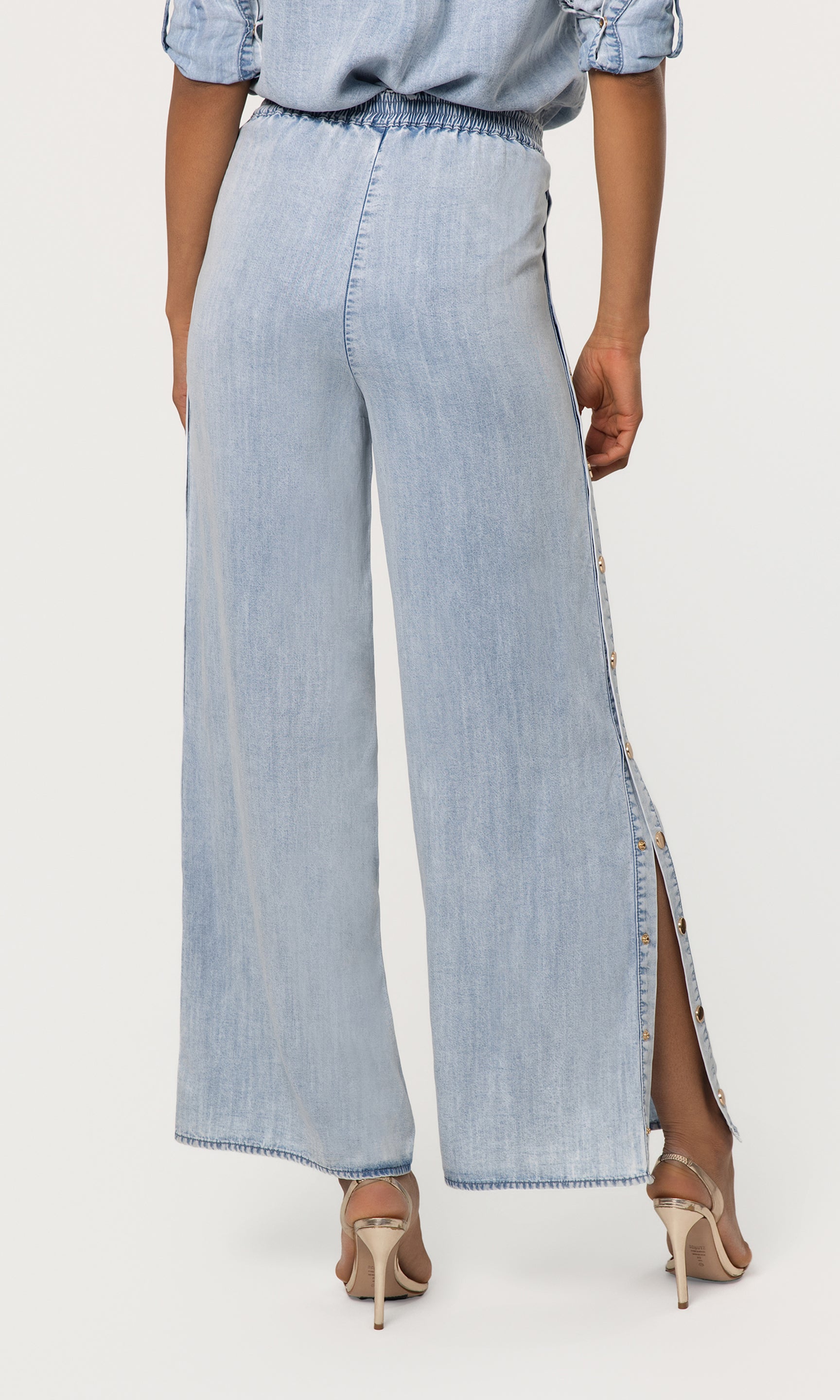 Back view of light blue denim pants with a side slit worn by a person on a white background