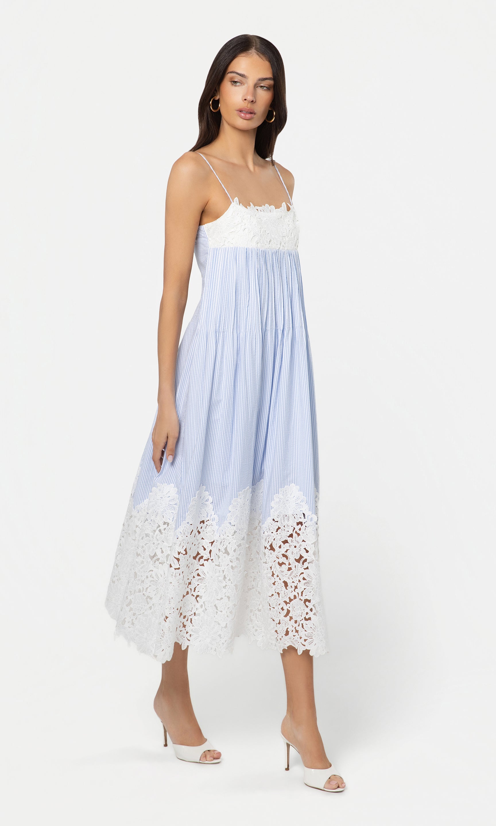 Side view of woman wearing a light blue and white dress with lace details on a white background