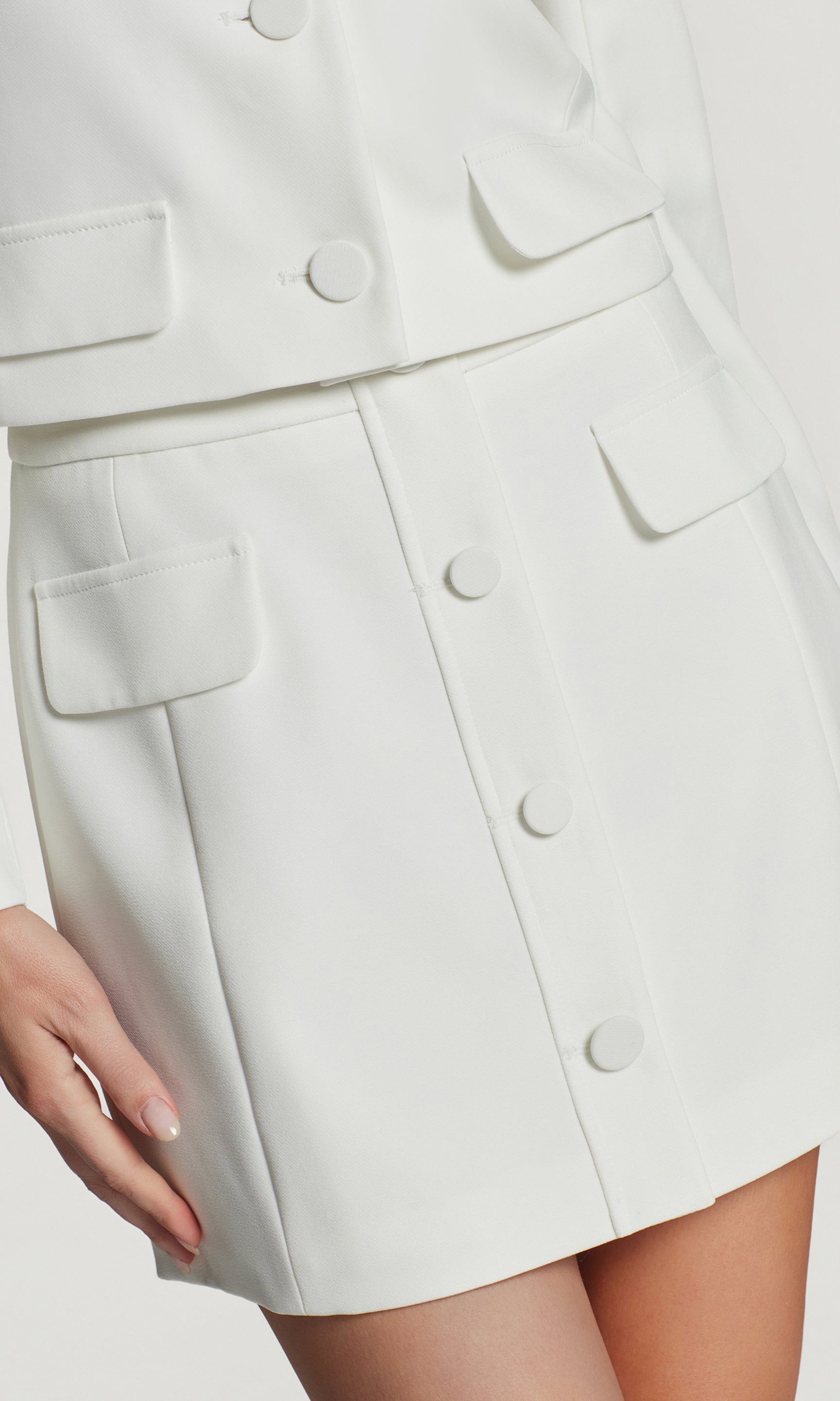 Close-up of white skirt with button details on a light gray background