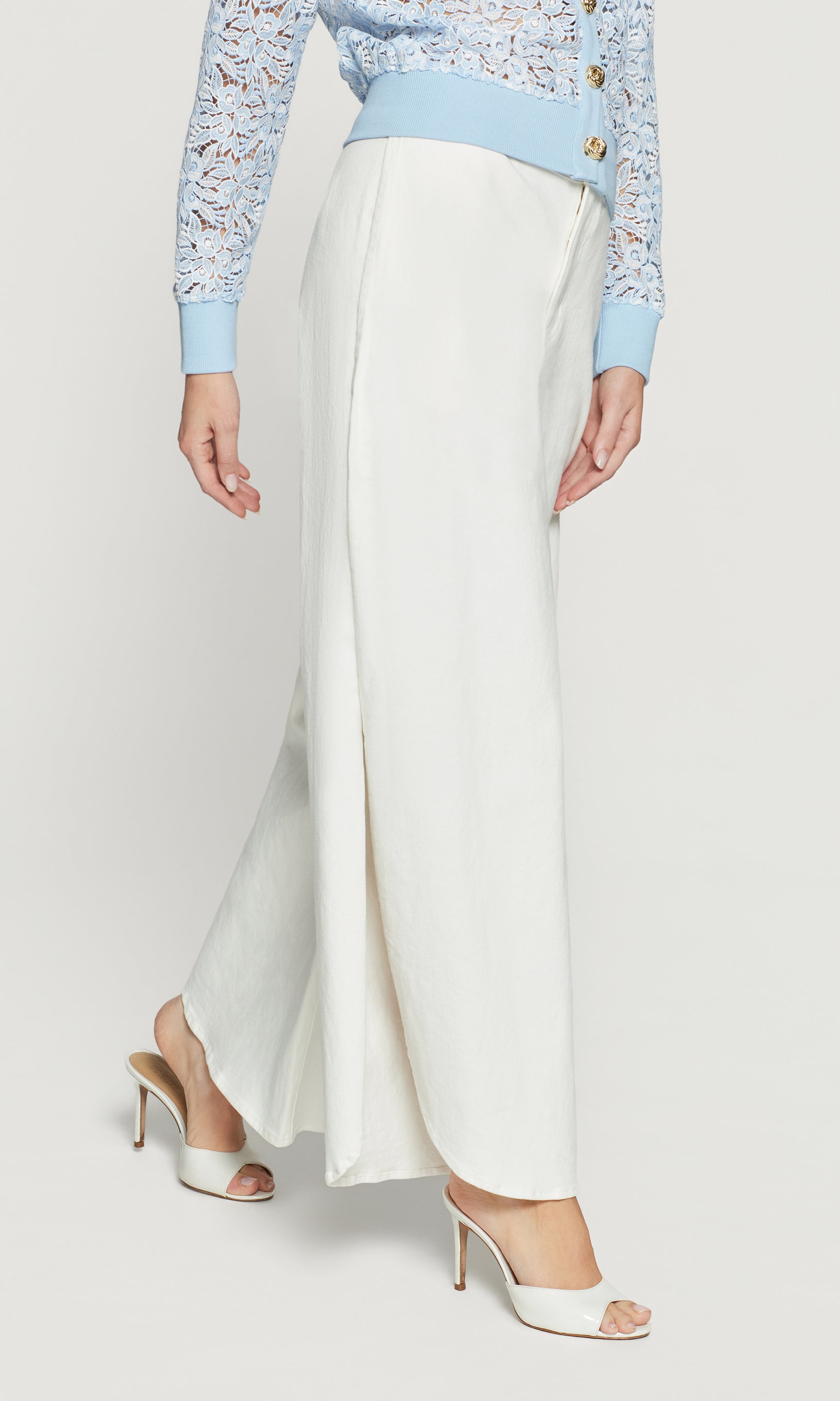 Side view of person wearing a light blue top with floral patterns and white wide-leg pants on a plain background