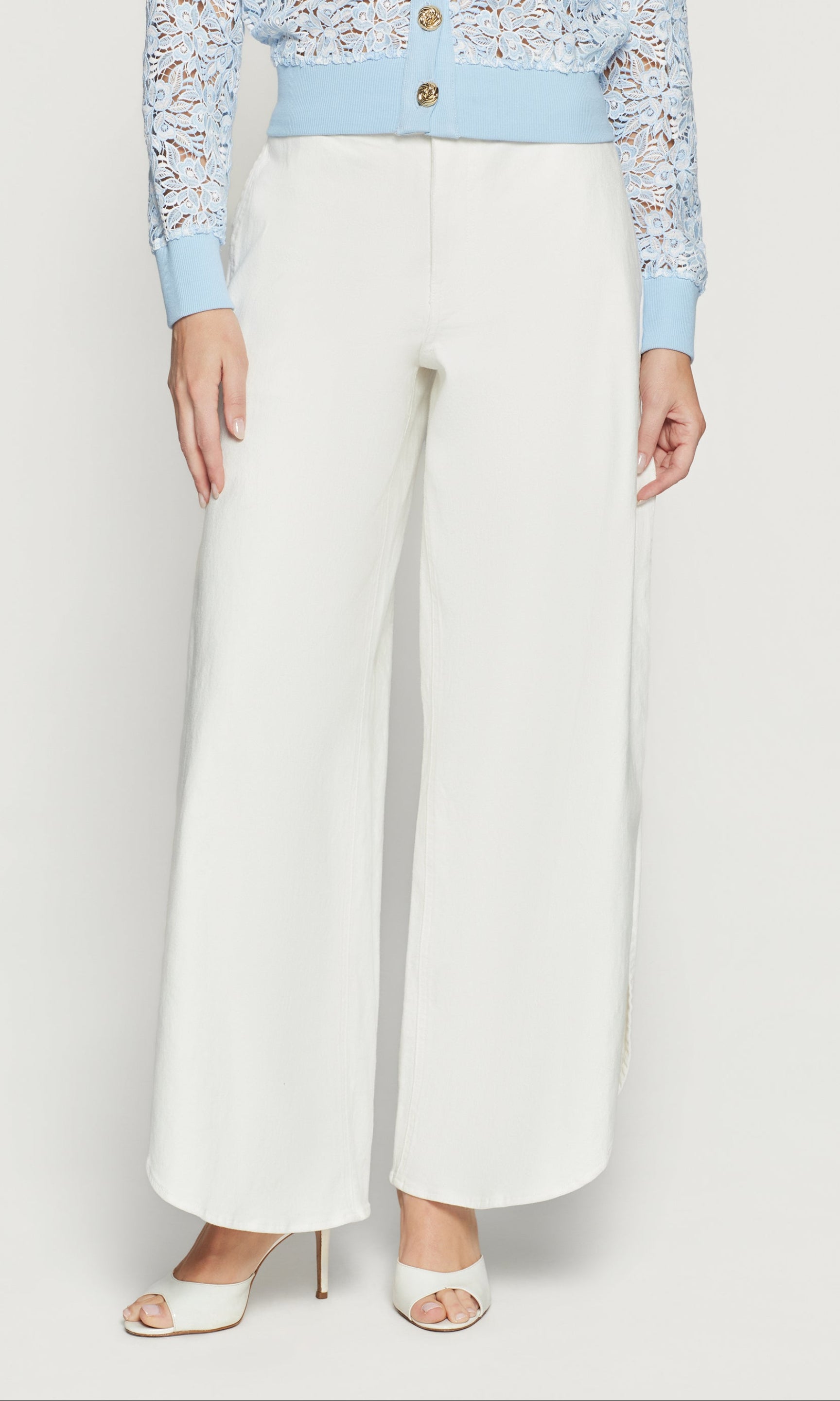 Person wearing a light blue lace top and white wide-leg pants on a white background