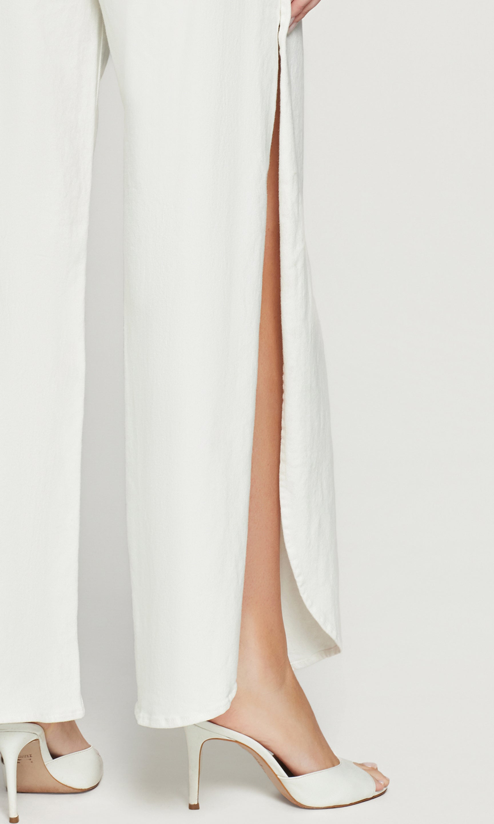 White pants with a high slit and white high-heeled shoes on a light background