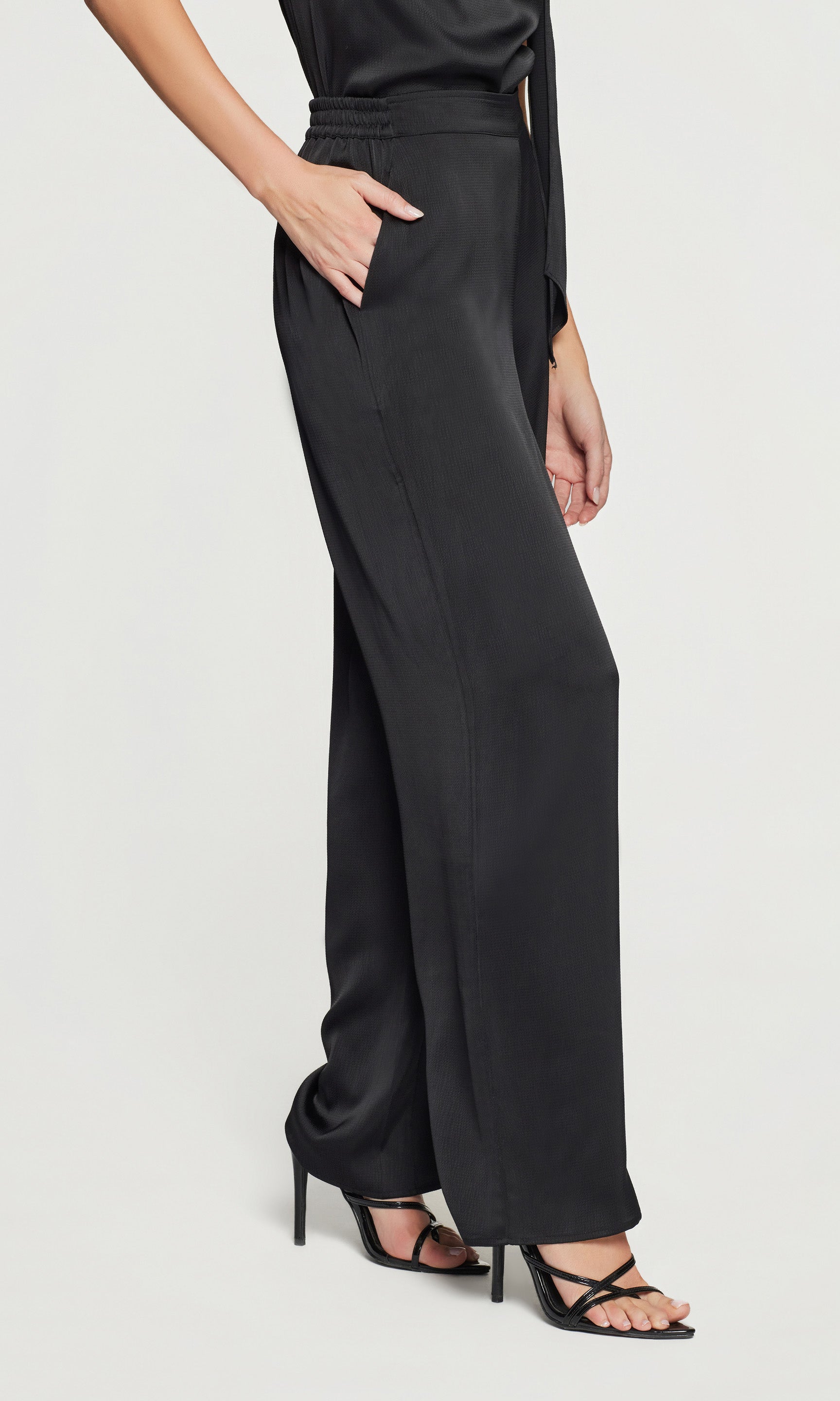 Side view of black wide-leg pants worn by a person on a light gray background
