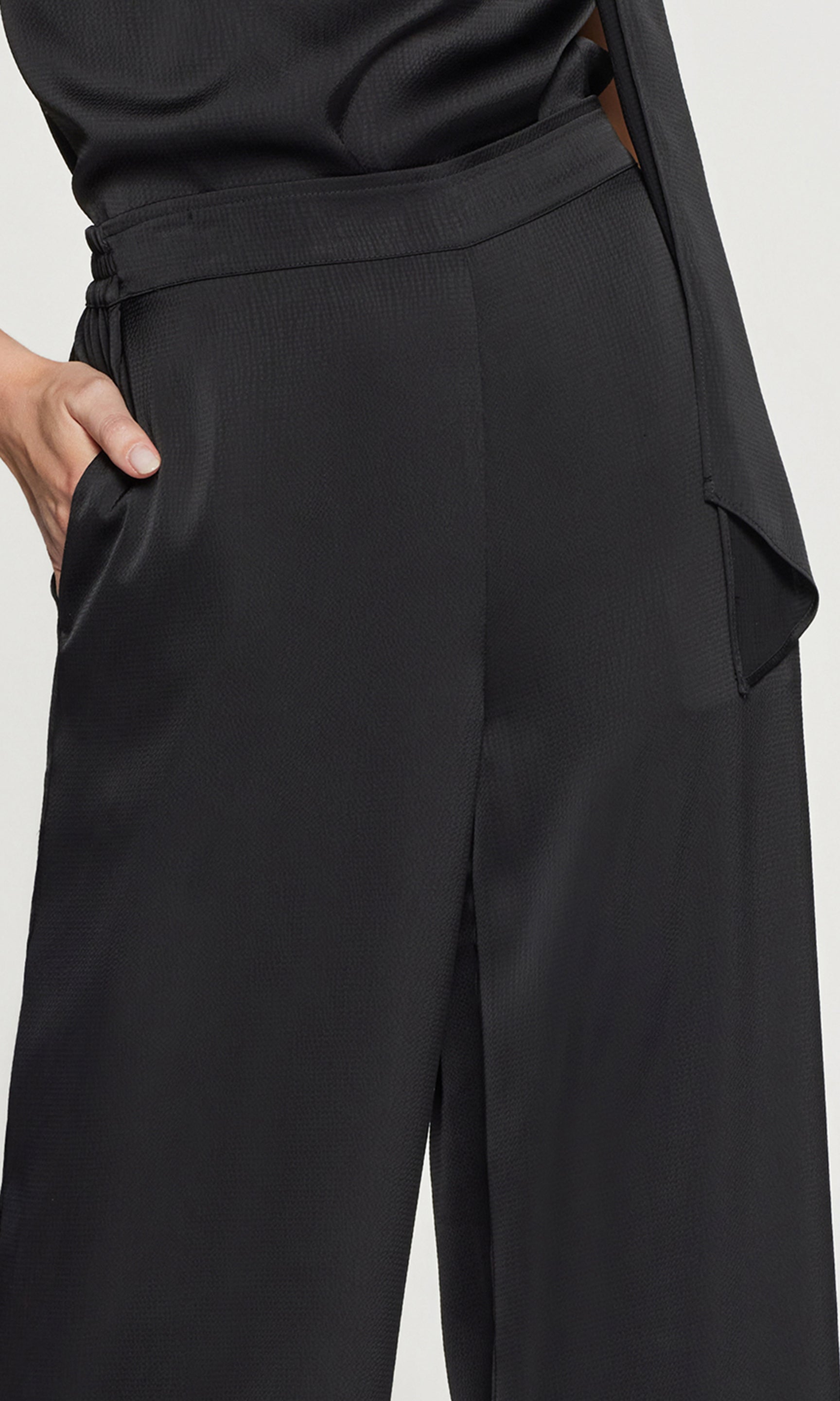 Close-up of black pants worn by a person on a light gray background