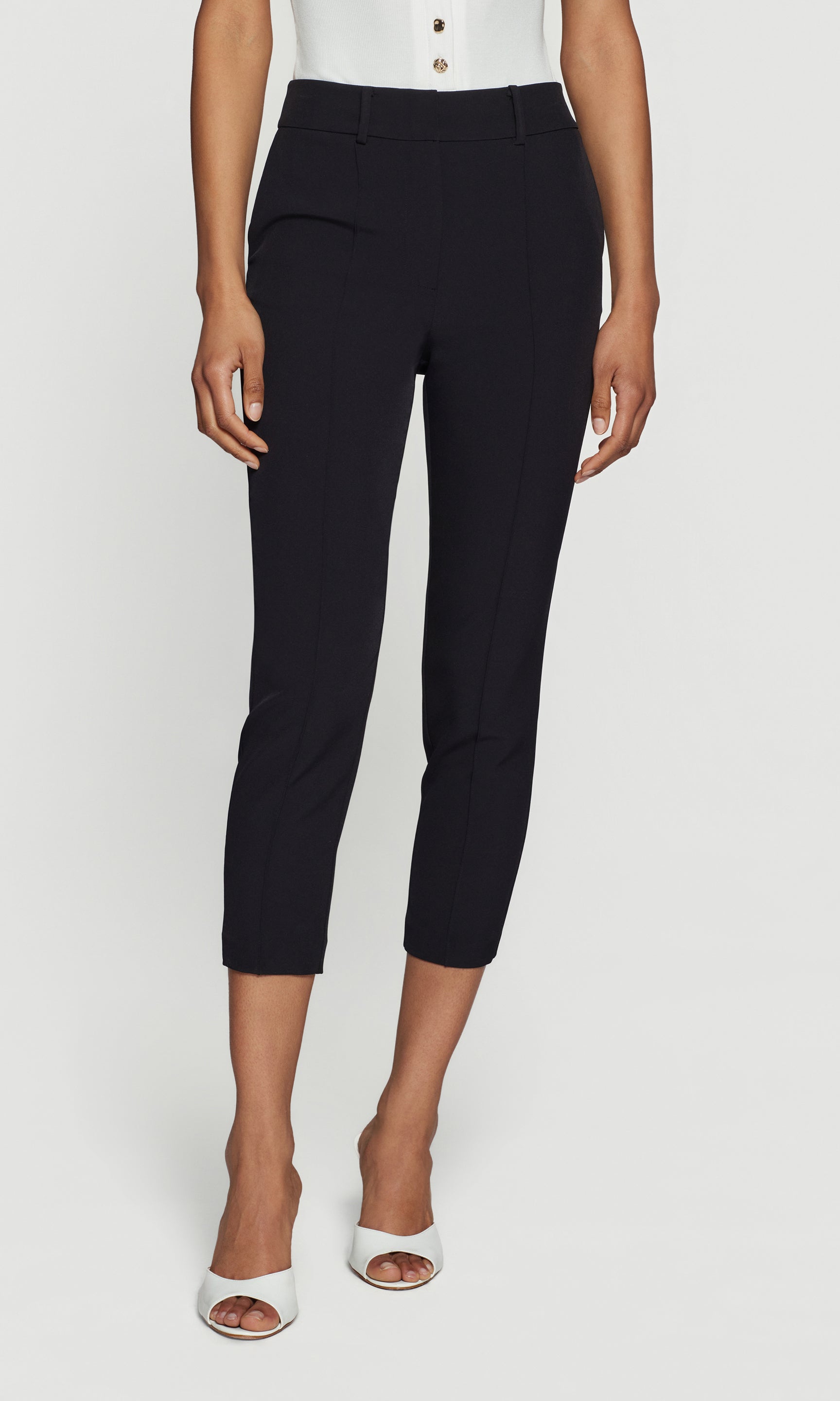 Person wearing black capri pants and white shoes on a white background