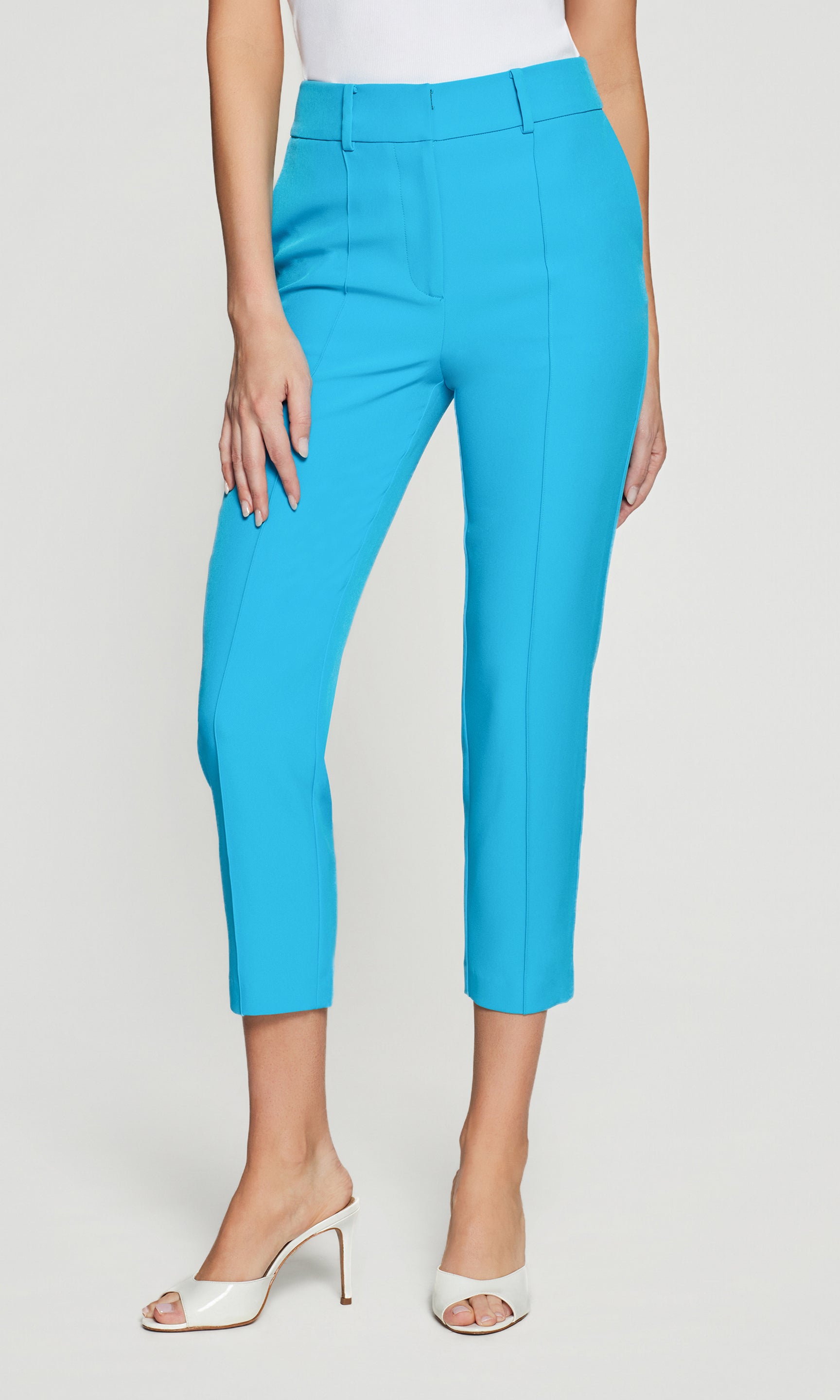 Turquoise capri pants worn by a person on a white background