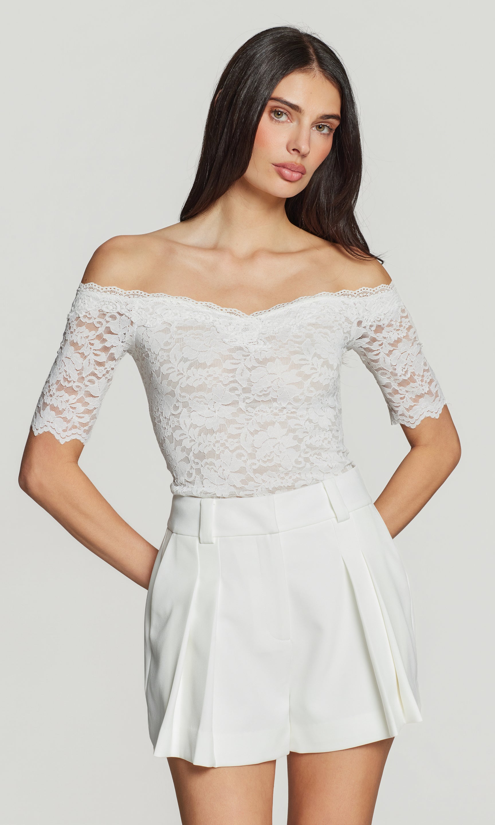 Woman wearing a white lace top and shorts on a plain background