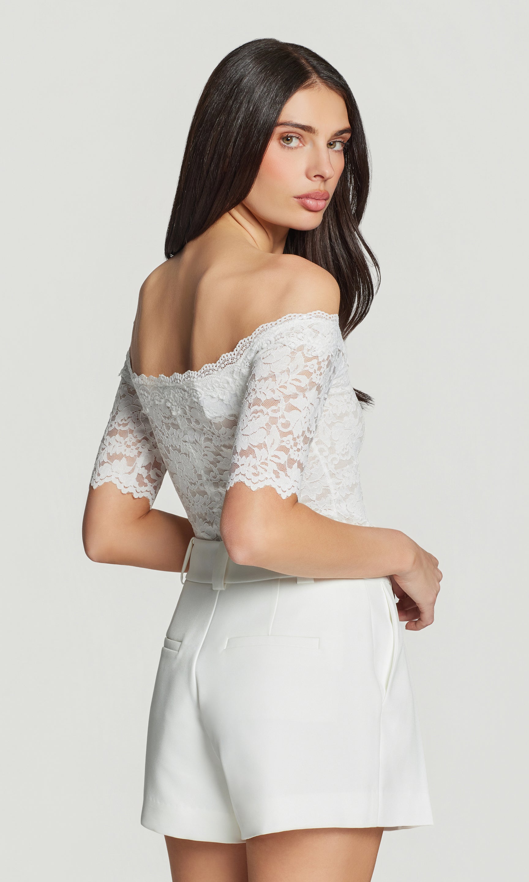 Woman wearing a white lace top and white shorts on a light gray background